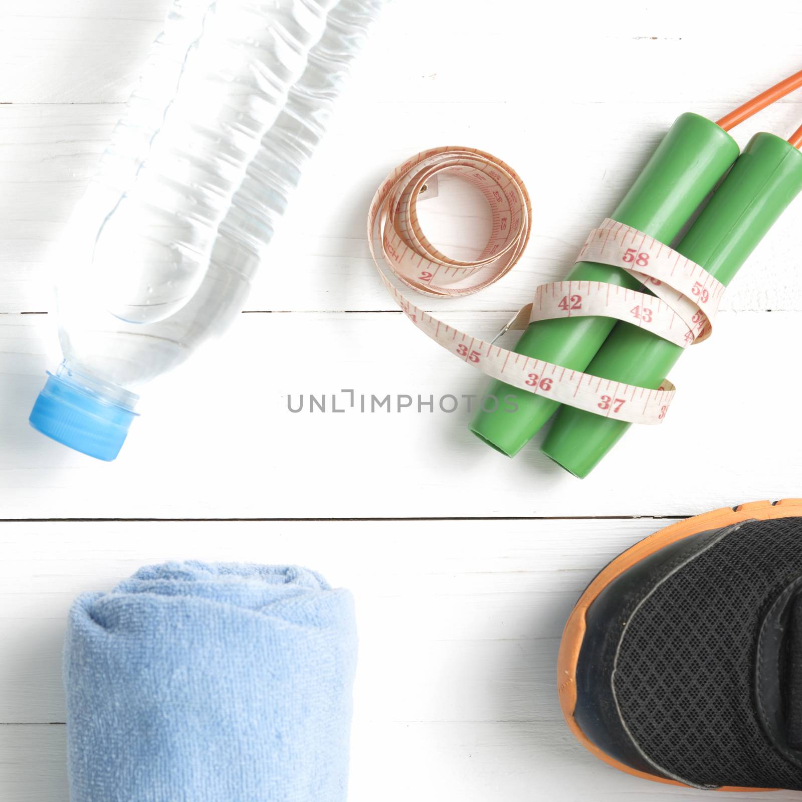 fitness equipment : running shoes,towel,jumping rope,water bottle and measuring tape on white wood table