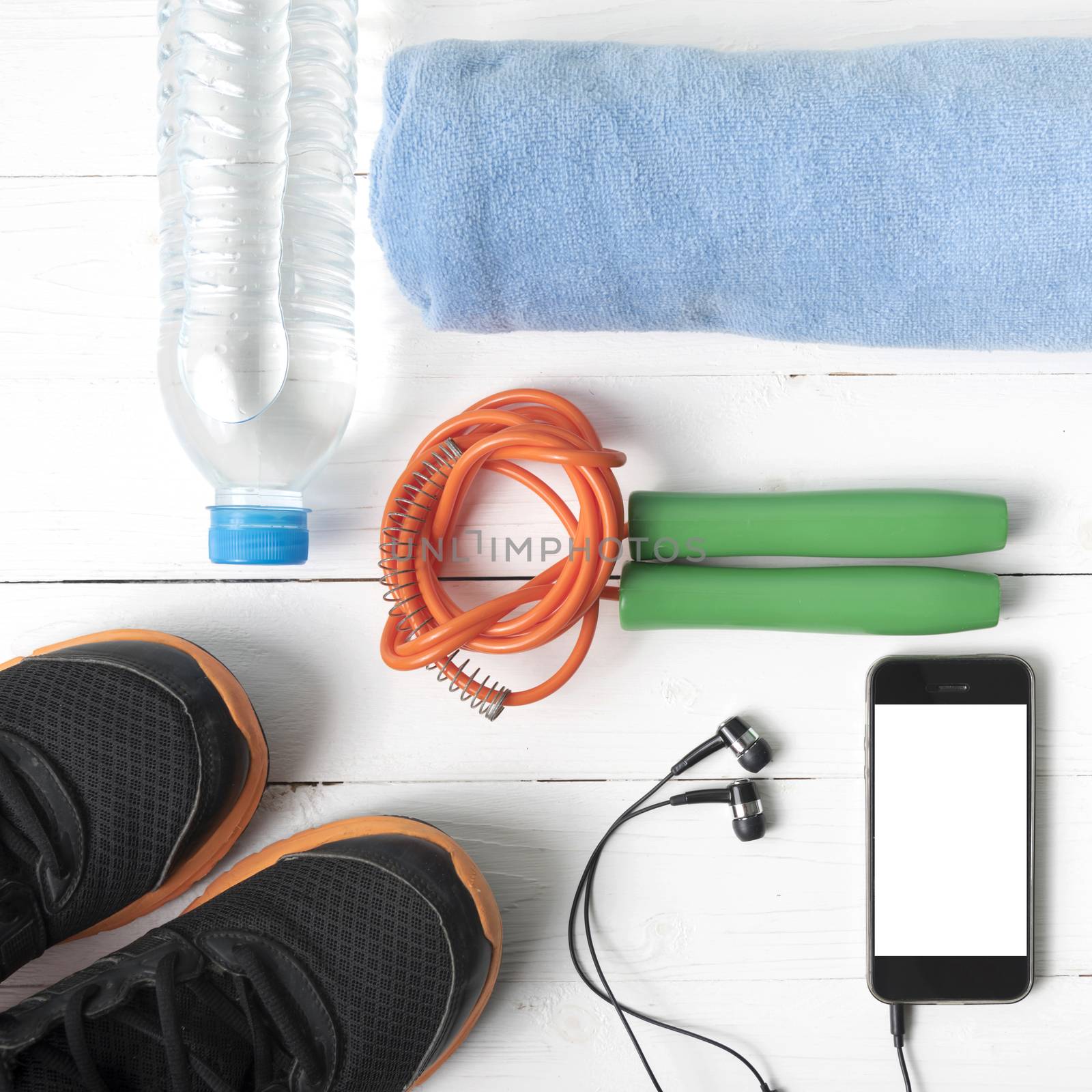 fitness equipment : running shoes,towel,jumping rope,water bottle and phone on white wood table