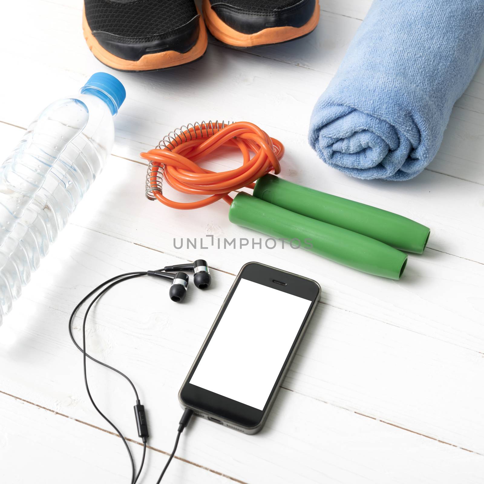fitness equipment : running shoes,towel,jumping rope,water bottle and phone on white wood table