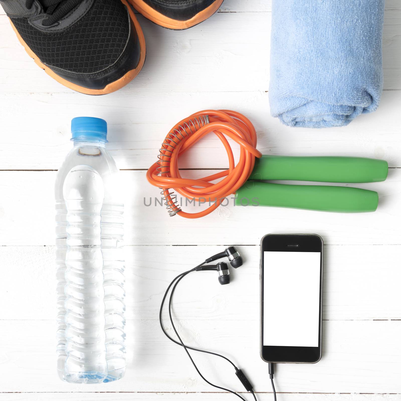 fitness equipment : running shoes,towel,jumping rope,water bottle and phone on white wood table