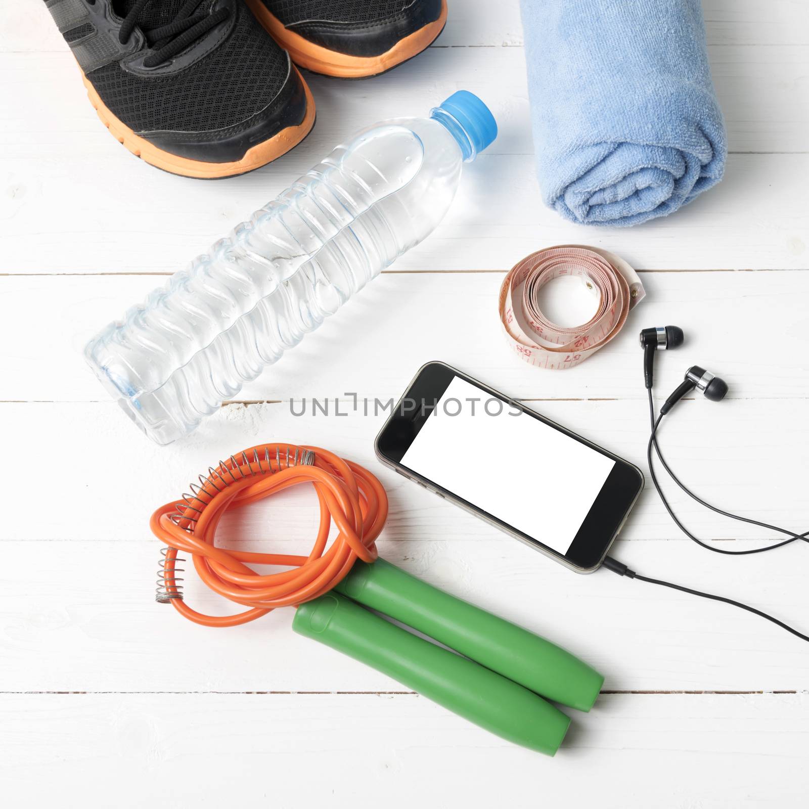 fitness equipment : running shoes,towel,jumping rope,water bottle,phone and measuring tape on white wood table