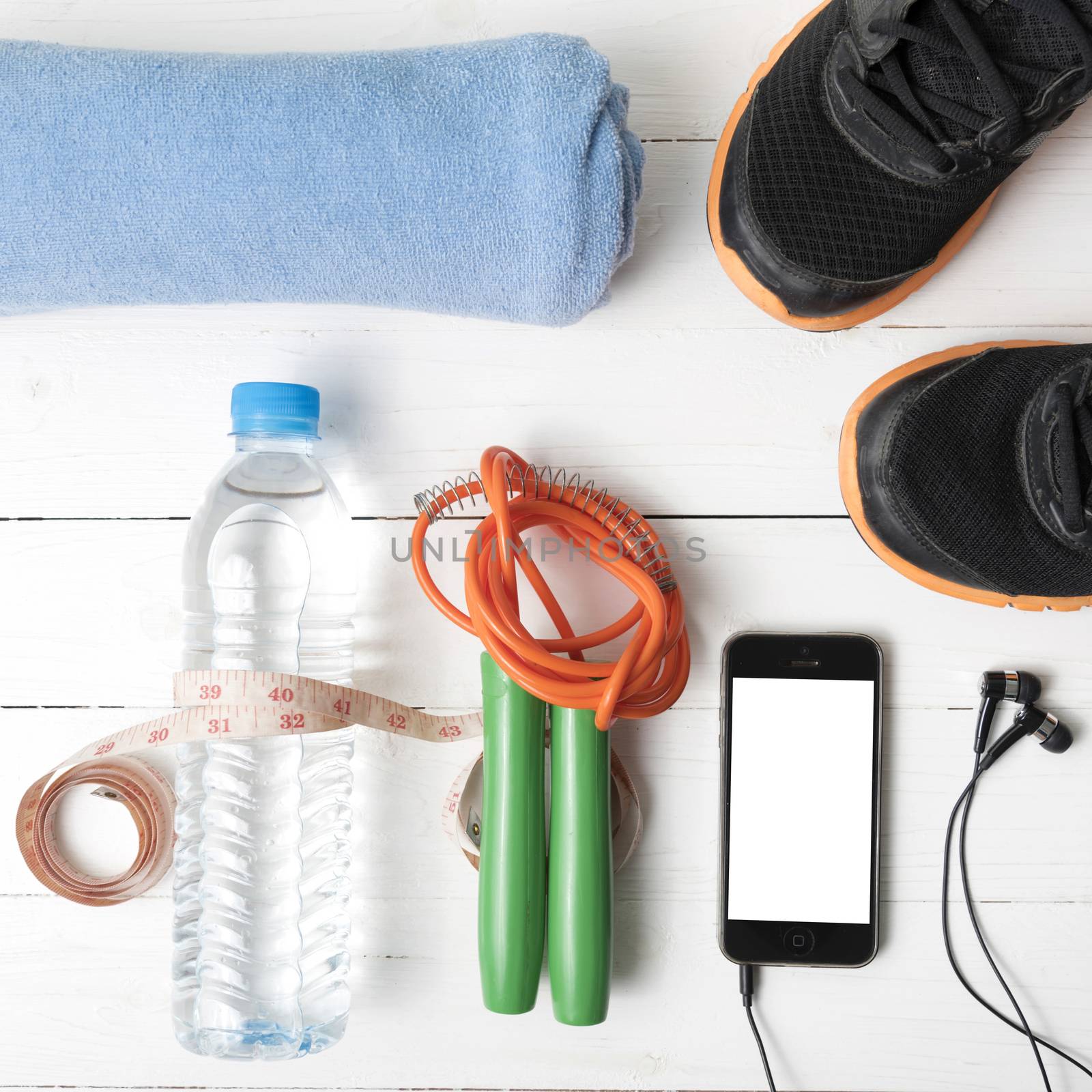 fitness equipment : running shoes,towel,jumping rope,water bottle,phone and measuring tape on white wood table