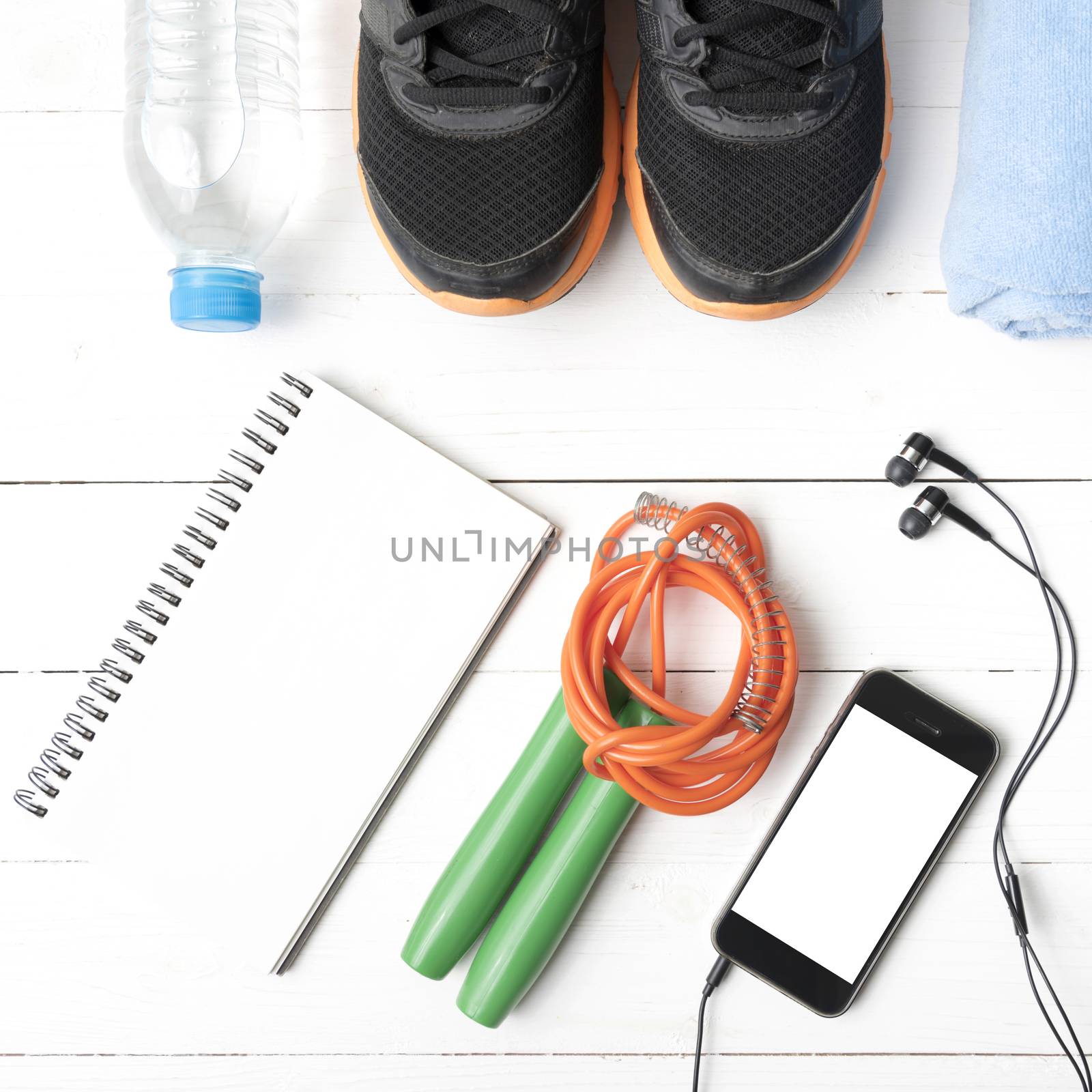 fitness equipment : running shoes,towel,jumping rope,water bottle,phone and notepad on white wood table