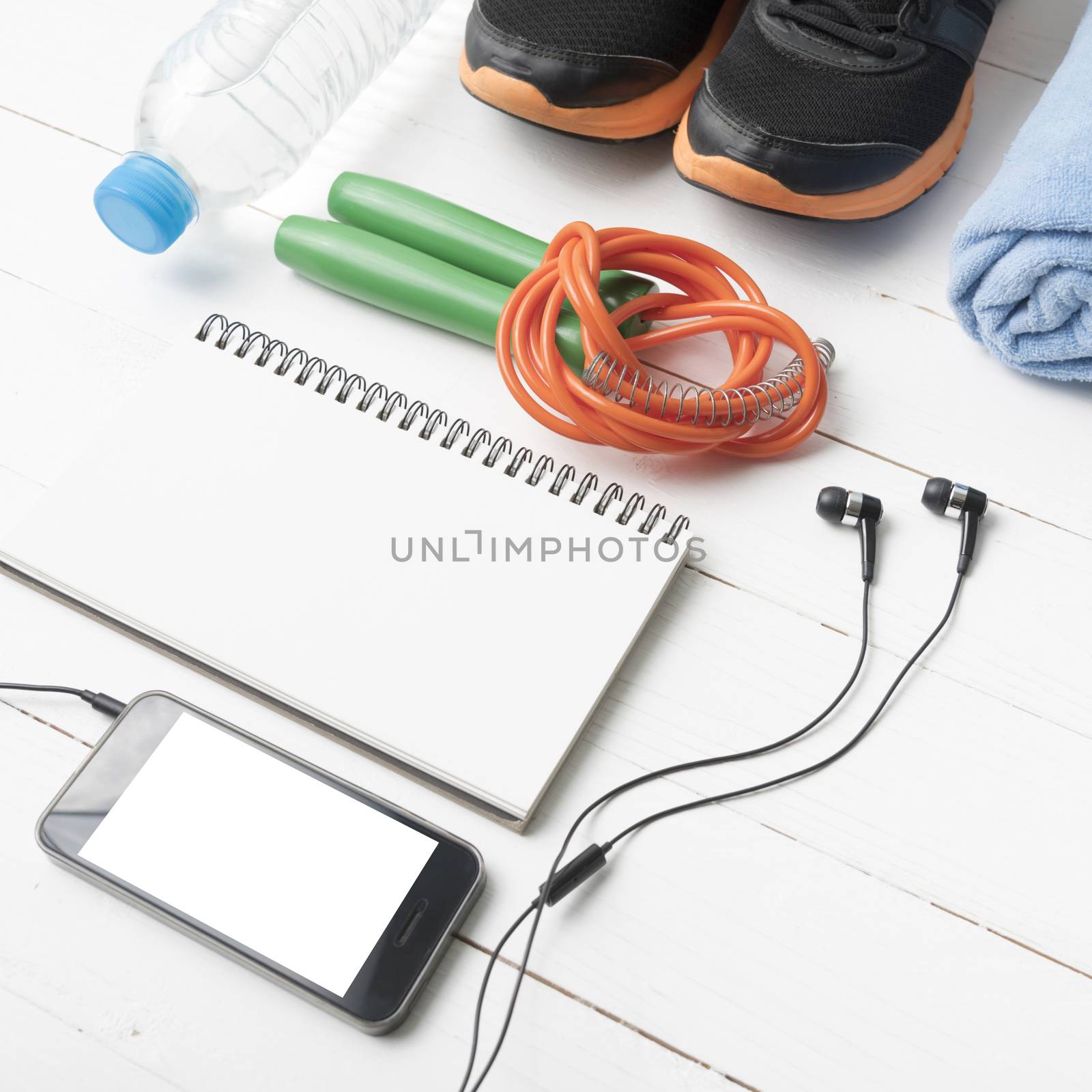 fitness equipment : running shoes,towel,jumping rope,water bottle,phone and notepad on white wood table