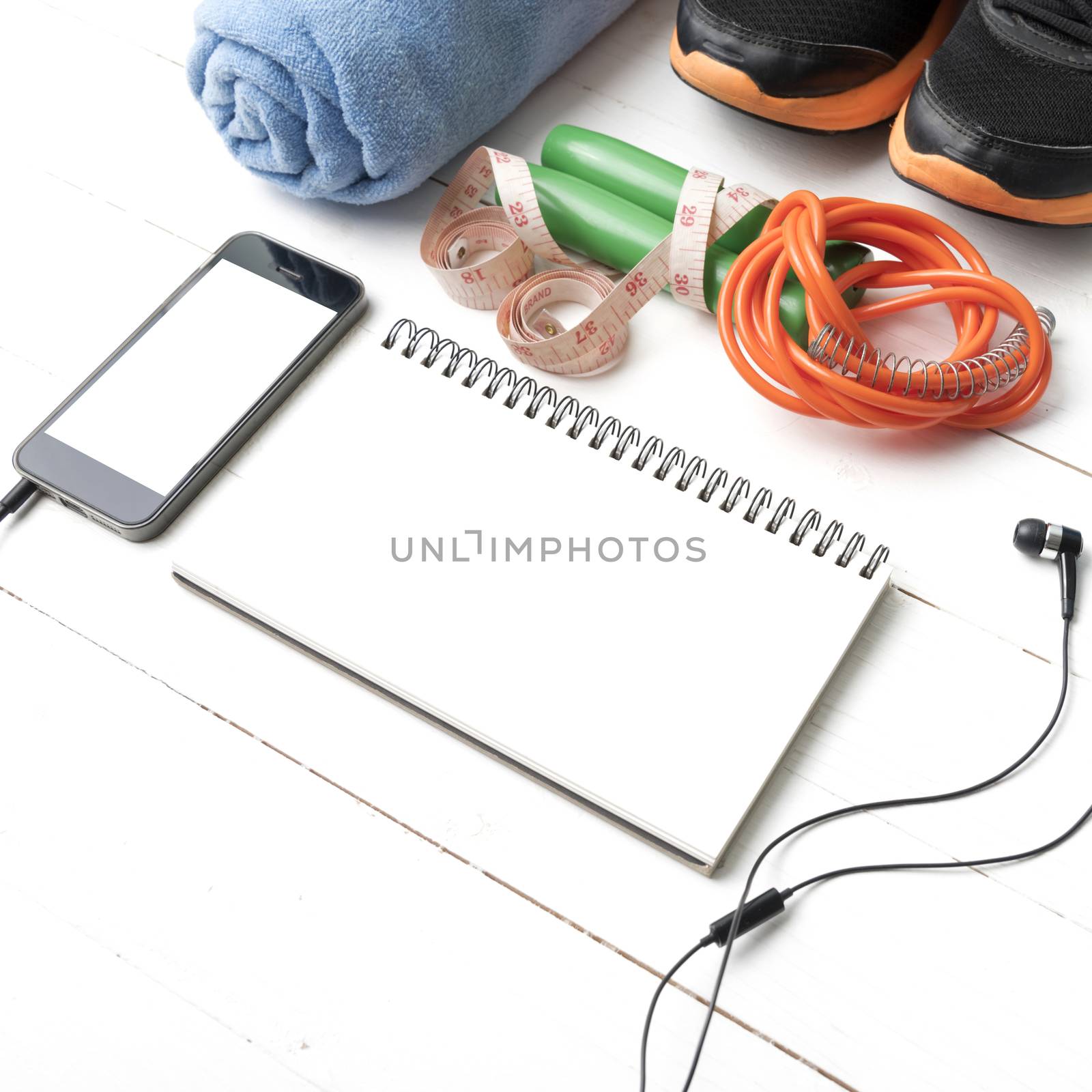 fitness equipment : running shoes,towel,jumping rope,phone,notepad and measuring tape on white wood table