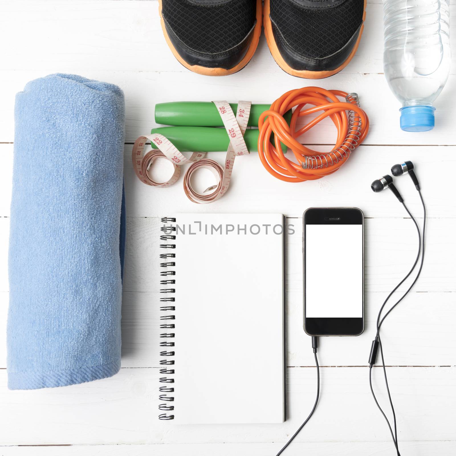 fitness equipment : running shoes,towel,jumping rope,water bottle,phone,notepad and measuring tape on white wood table