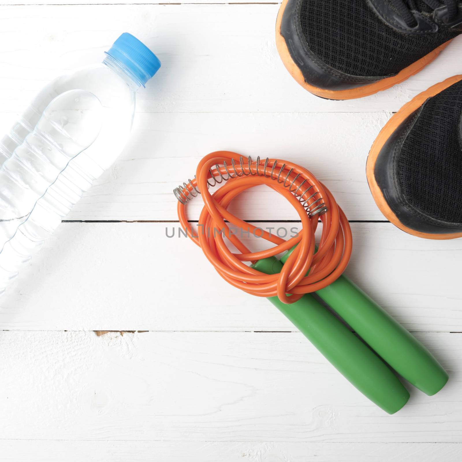 fitness equipment : running shoes,jumping rope and water bottle on white wood table