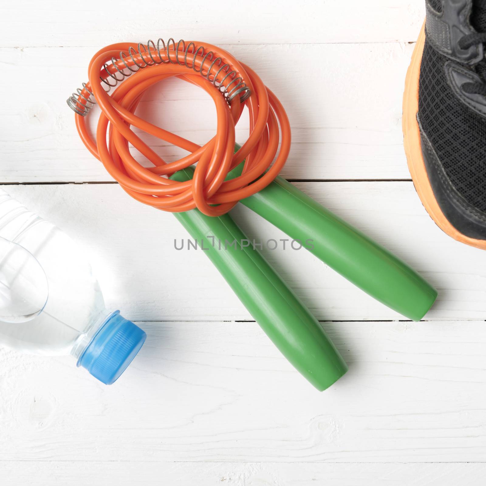 fitness equipment : running shoes,jumping rope and water bottle on white wood table