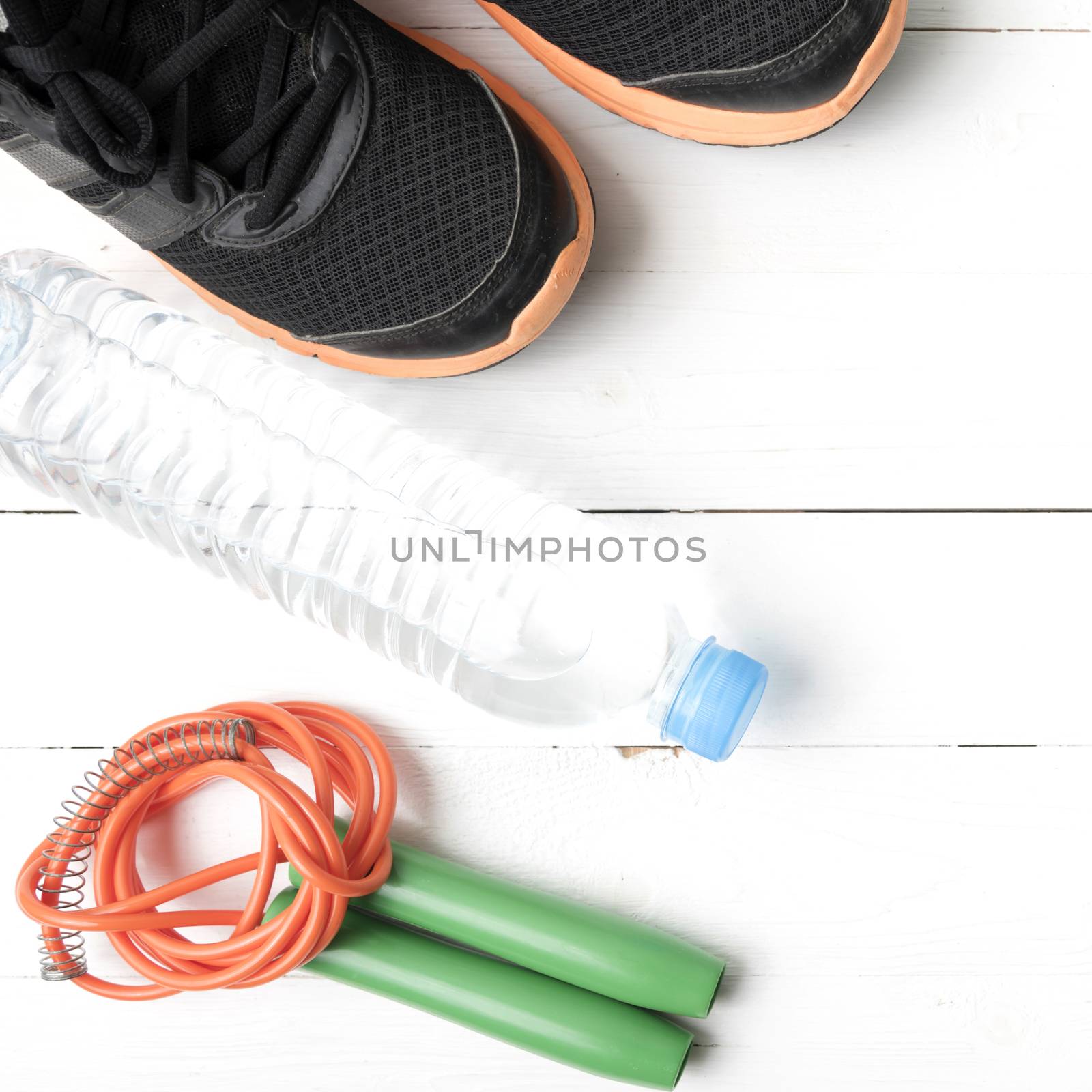 fitness equipment : running shoes,jumping rope,phone and water bottle on white wood table