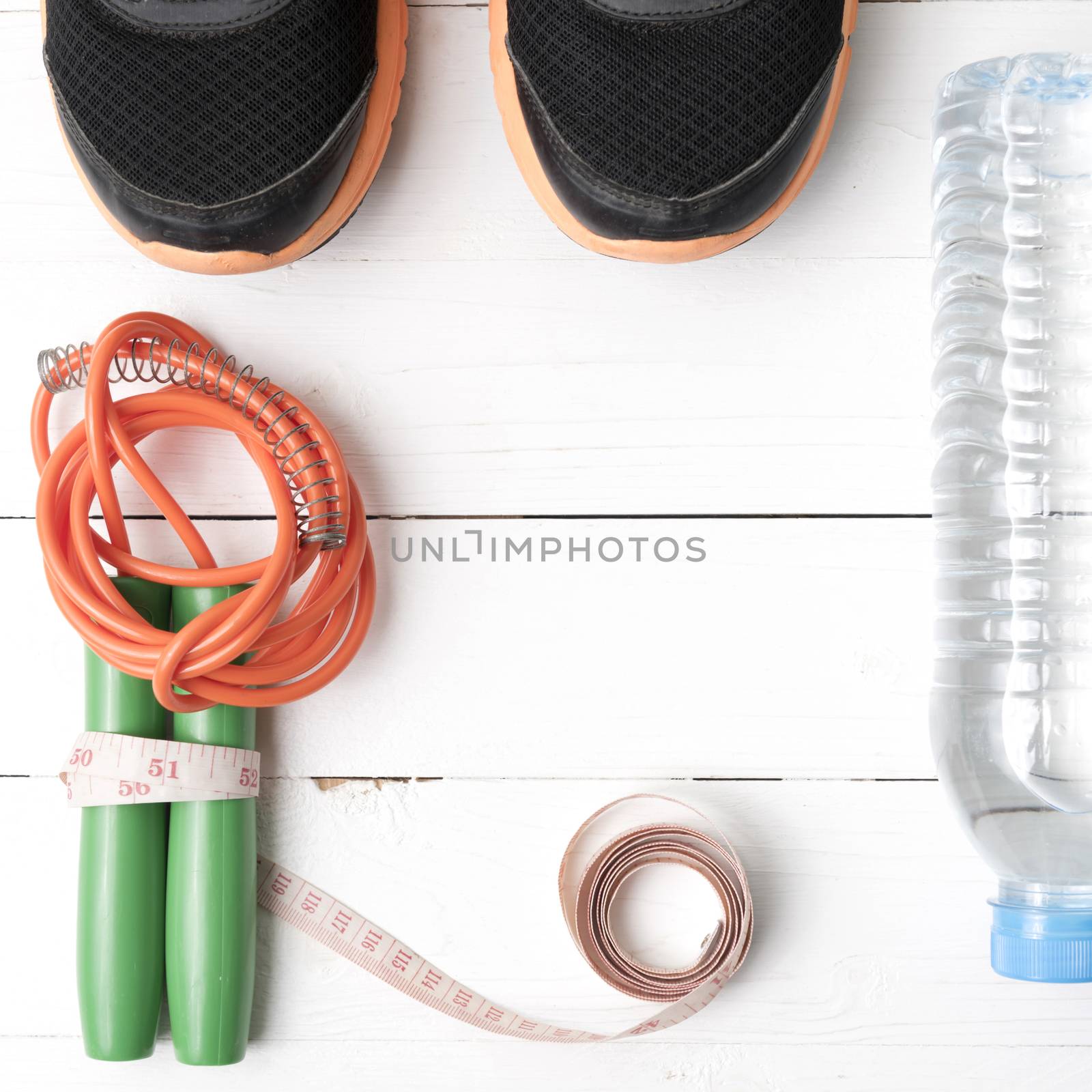 fitness equipment : running shoes,jumping rope,measuring tape and water bottle on white wood table