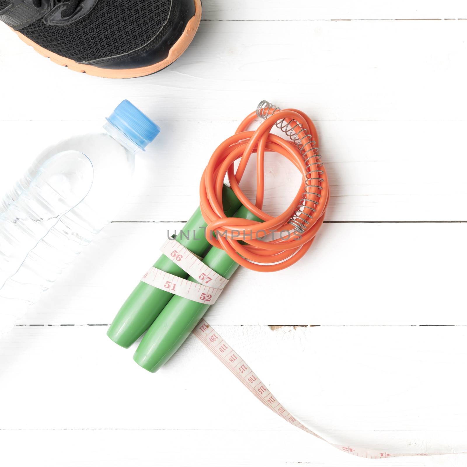 fitness equipment : running shoes,jumping rope,measuring tape and water bottle on white wood table