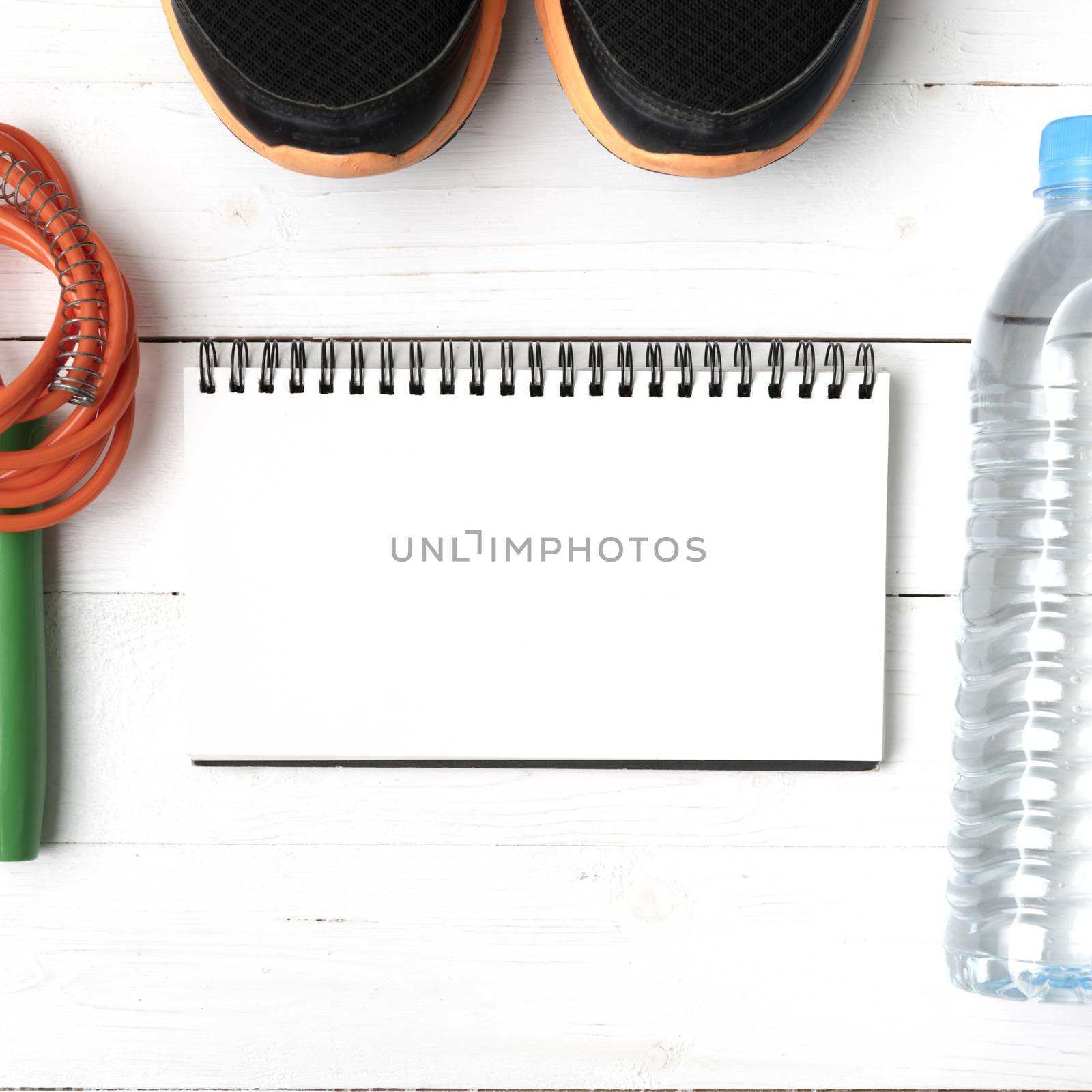 fitness equipment : running shoes,jumping rope,drinking water and notepad on white wood table