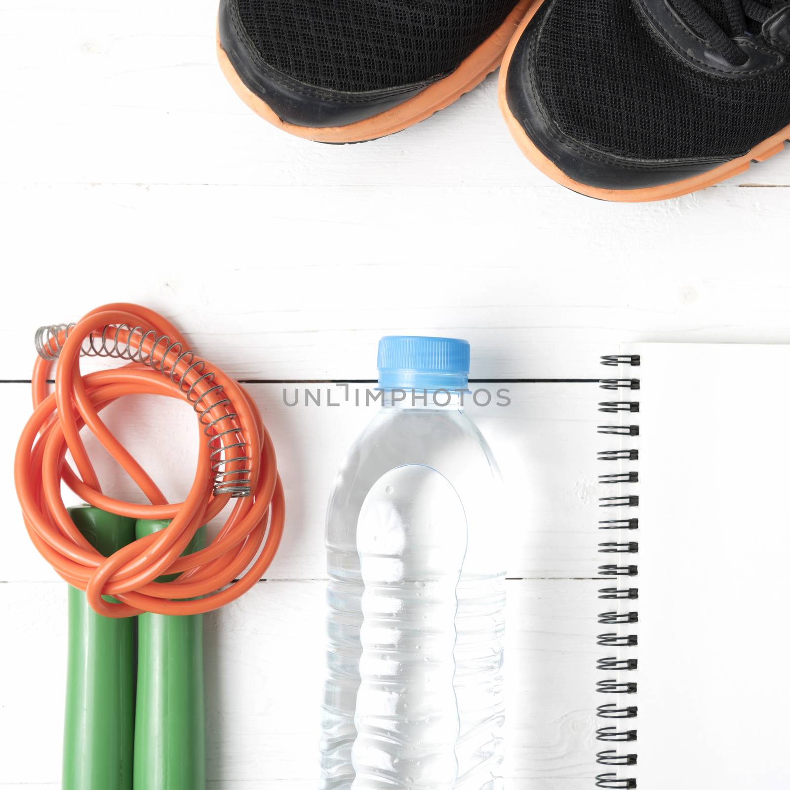 fitness equipment : running shoes,jumping rope,drinking water and notepad on white wood table