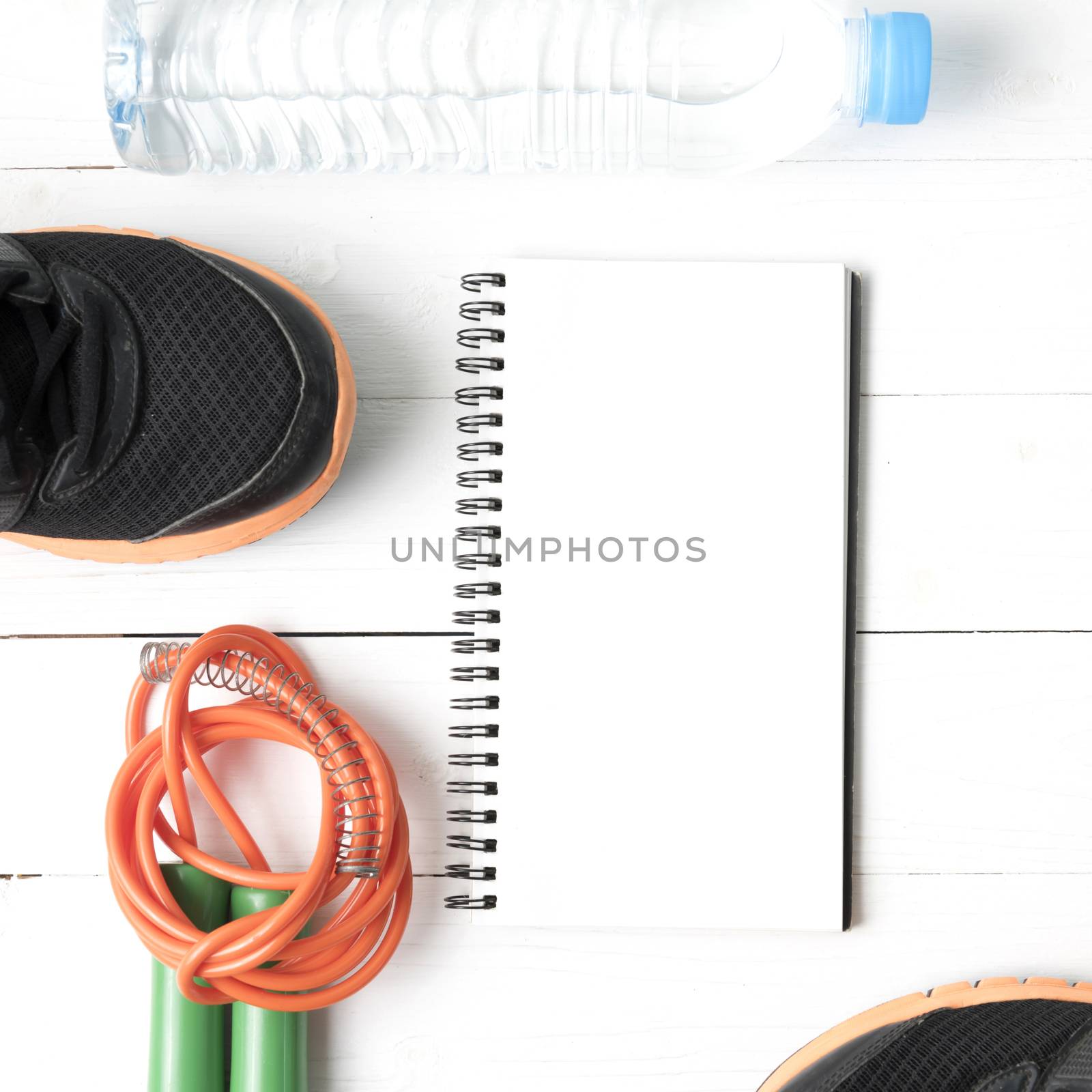 fitness equipment : running shoes,jumping rope,drinking water and notepad on white wood table