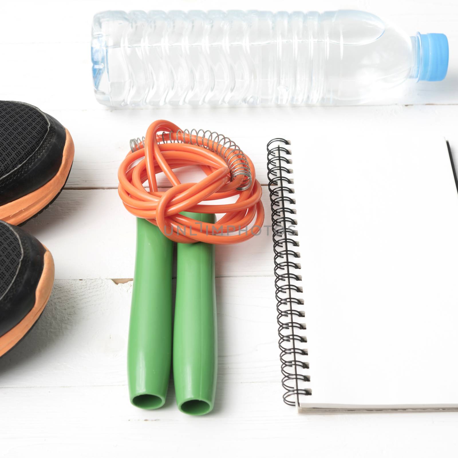 fitness equipment : running shoes,jumping rope,drinking water and notepad on white wood table