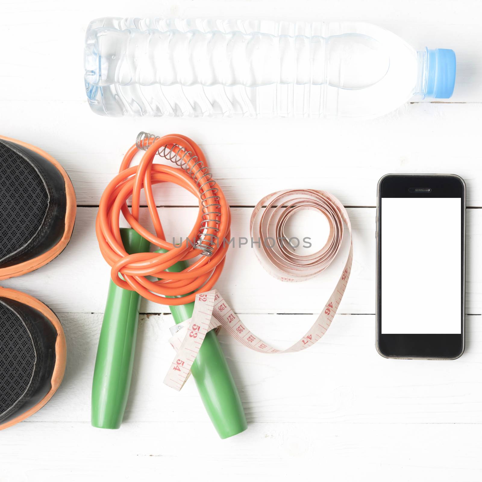 fitness equipment : running shoes,jumping rope,drinking water,measuring tape and phone on white wood table