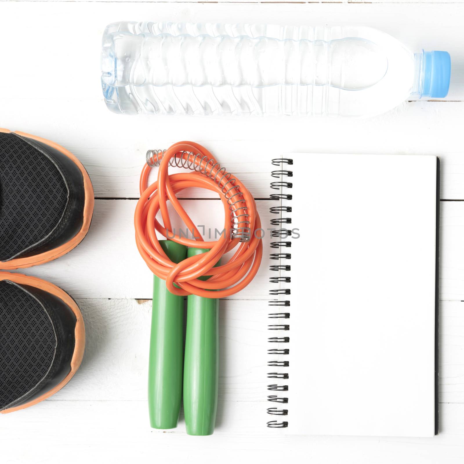 fitness equipment : running shoes,jumping rope,drinking water and notepad on white wood table