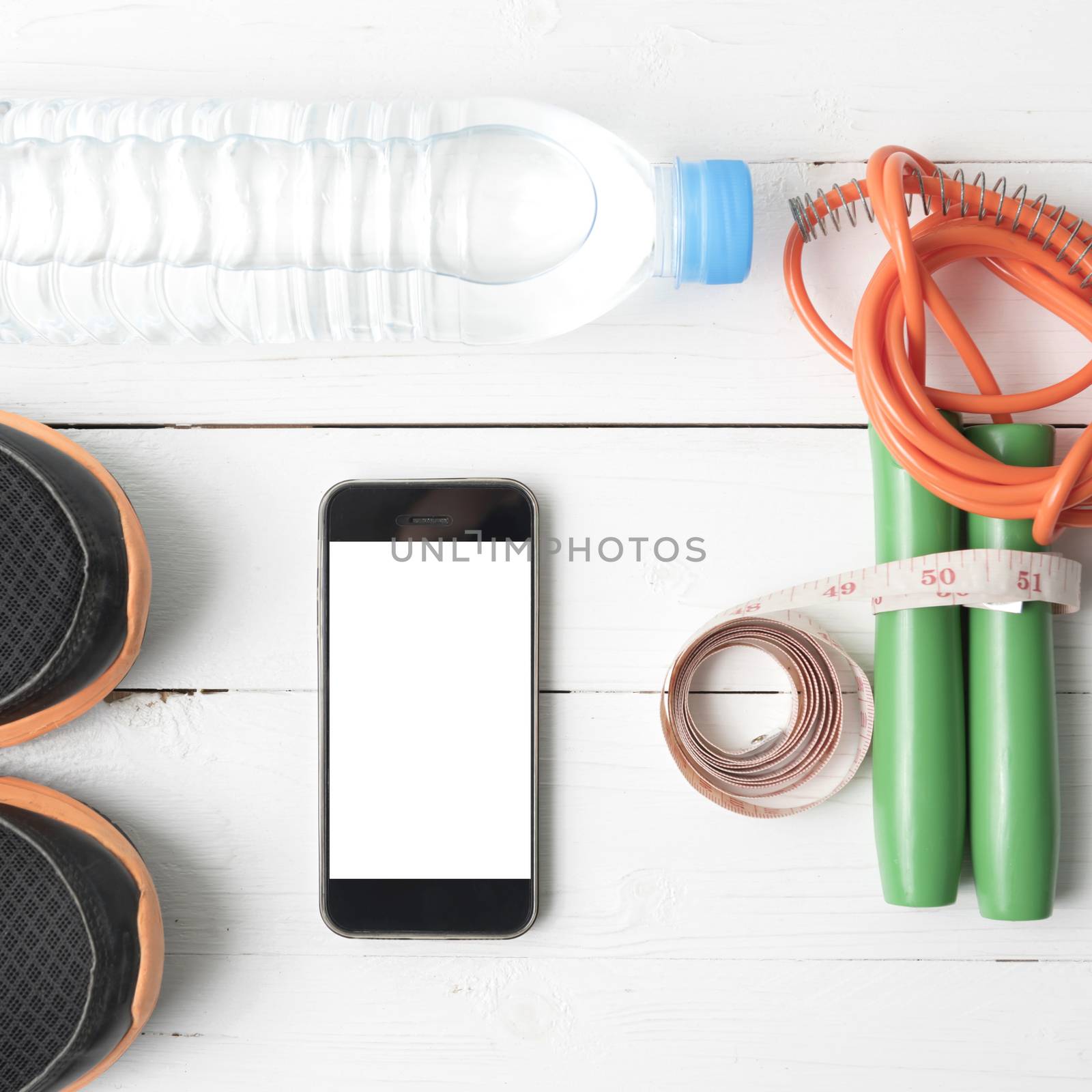 fitness equipment : running shoes,jumping rope,drinking water,measuring tape and phone on white wood table