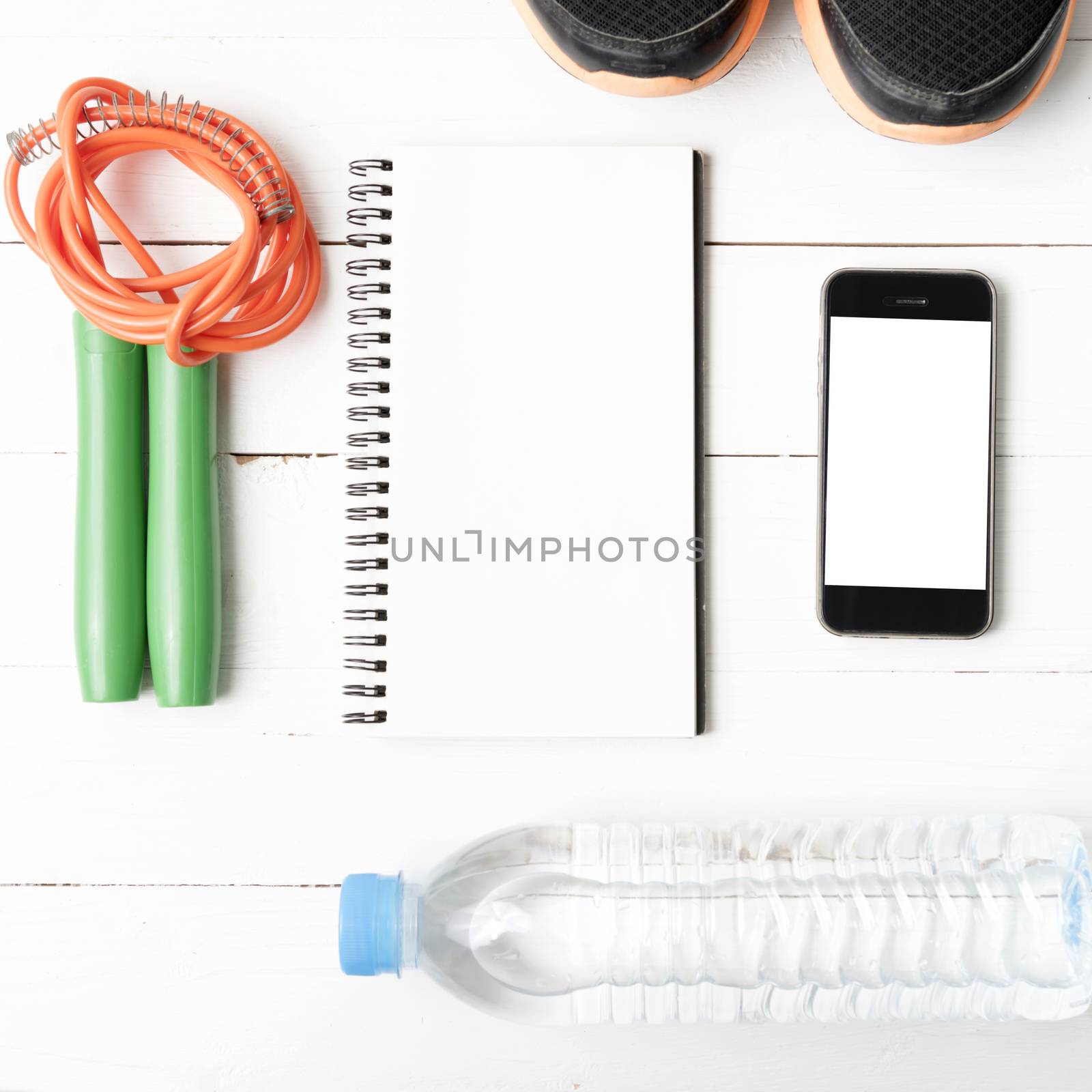 fitness equipment : running shoes,jumping rope,drinking water,notebook and phone on white wood table