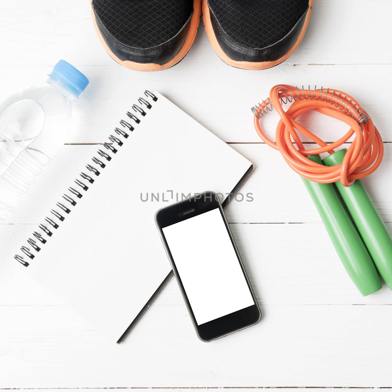 fitness equipment : running shoes,jumping rope,drinking water,notebook and phone on white wood table