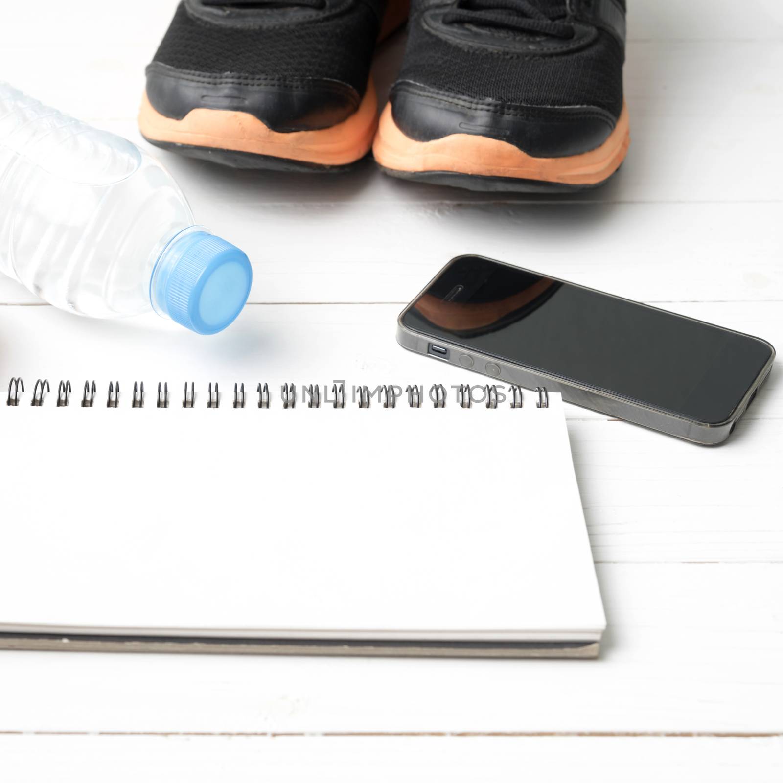 fitness equipment : running shoes,drinking water,notebook and phone on white wood table