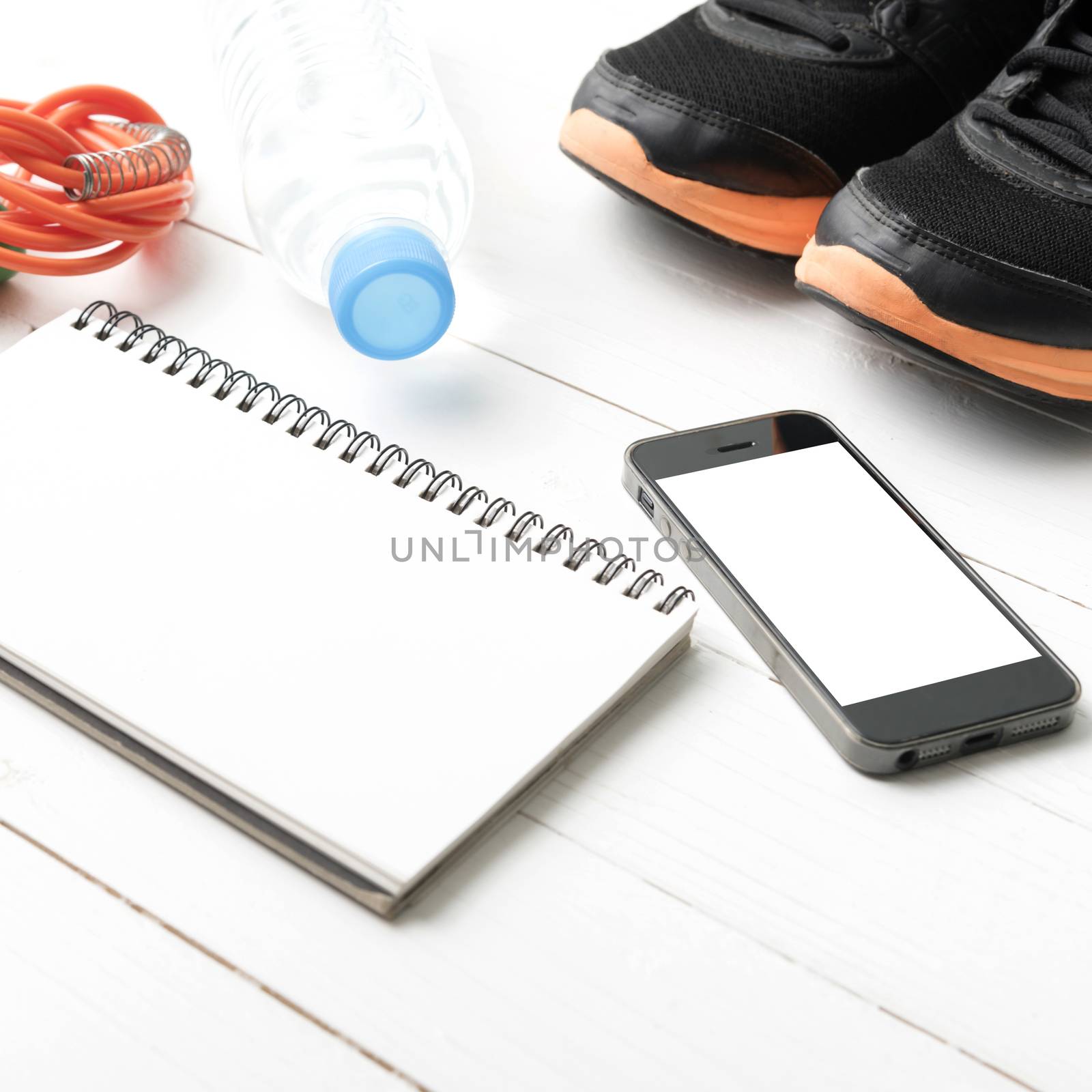 fitness equipment : running shoes,jumping rope,drinking water,notebook and phone on white wood table