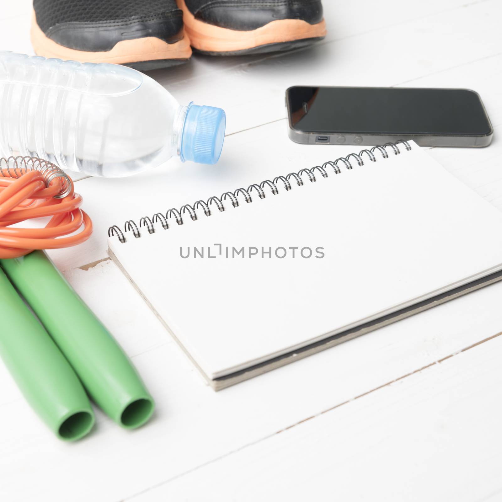 fitness equipment : running shoes,jumping rope,drinking water,notebook and phone on white wood table