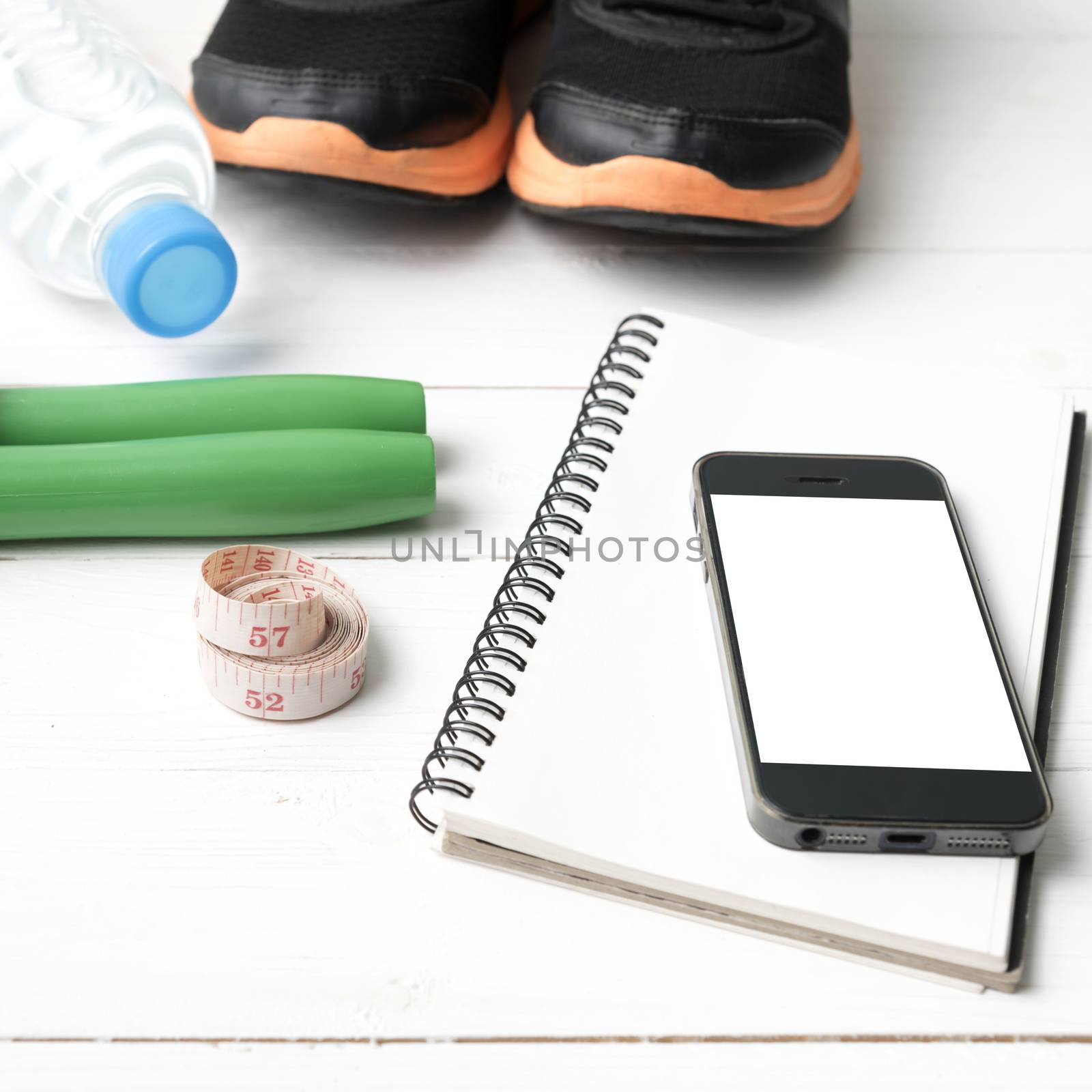 fitness equipment : running shoes,jumping rope,drinking water,notebook,measuring tape and phone on white wood table