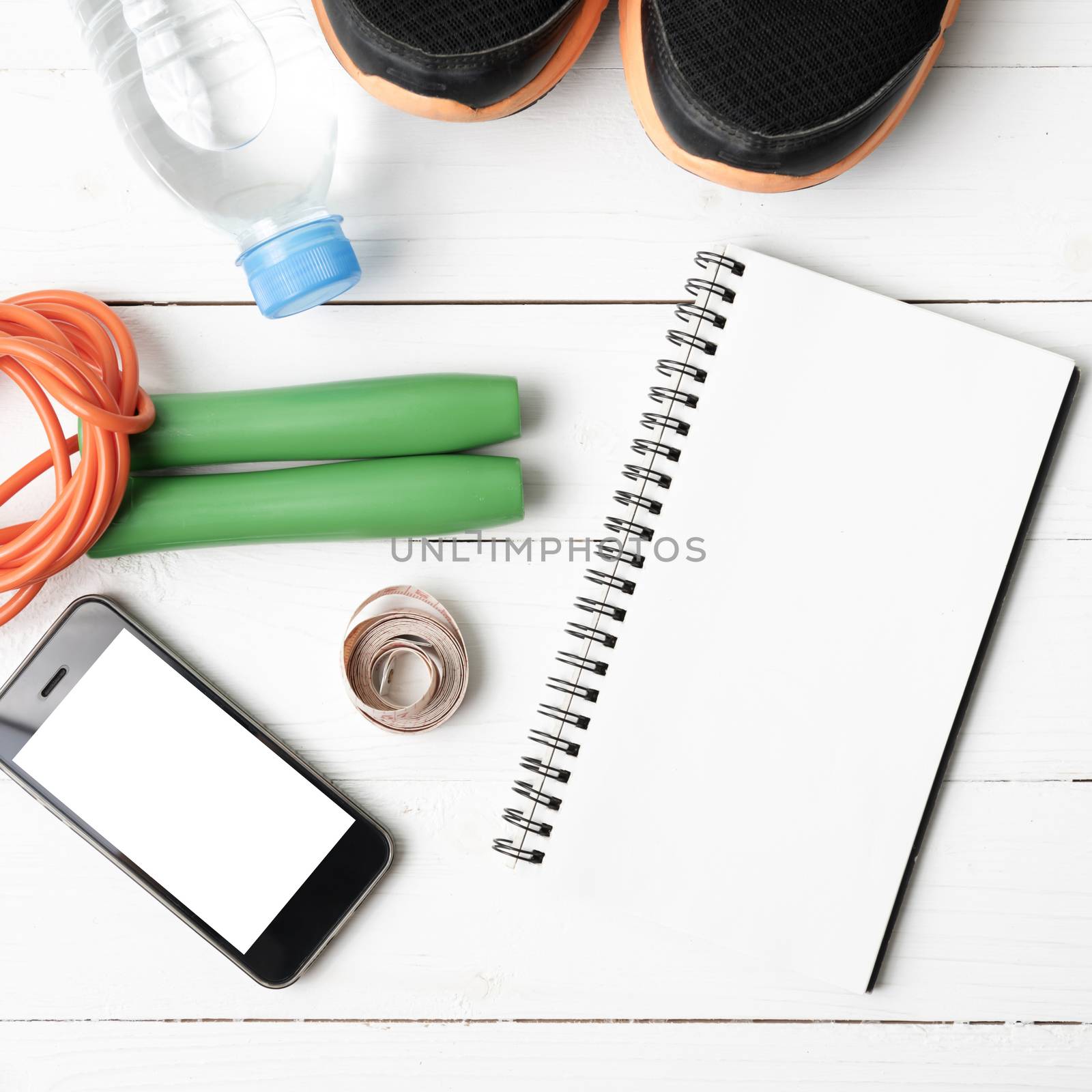 fitness equipment : running shoes,jumping rope,drinking water,notebook,measuring tape and phone on white wood table