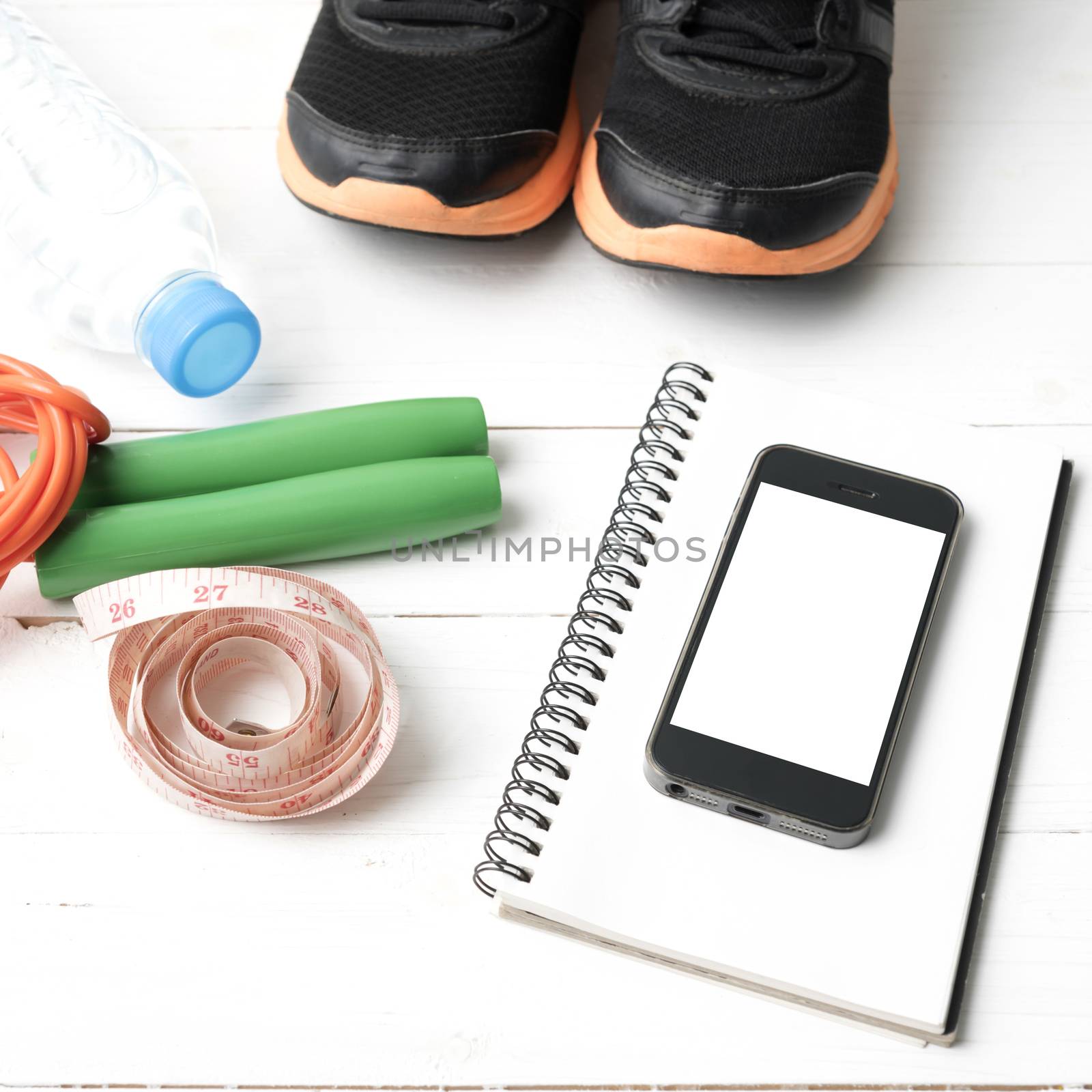 fitness equipment : running shoes,jumping rope,drinking water,notebook,measuring tape and phone on white wood table