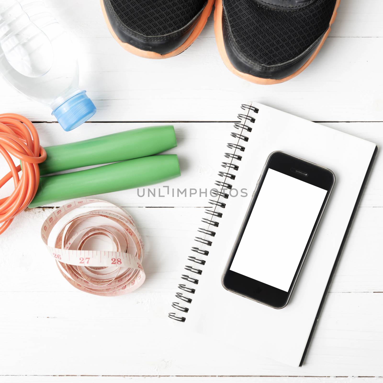 fitness equipment : running shoes,jumping rope,drinking water,notebook,measuring tape and phone on white wood table