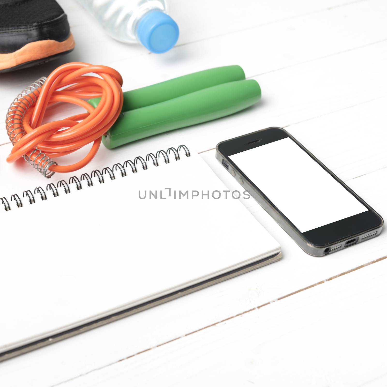 fitness equipment : running shoes,jumping rope,drinking water,notebook and phone on white wood table