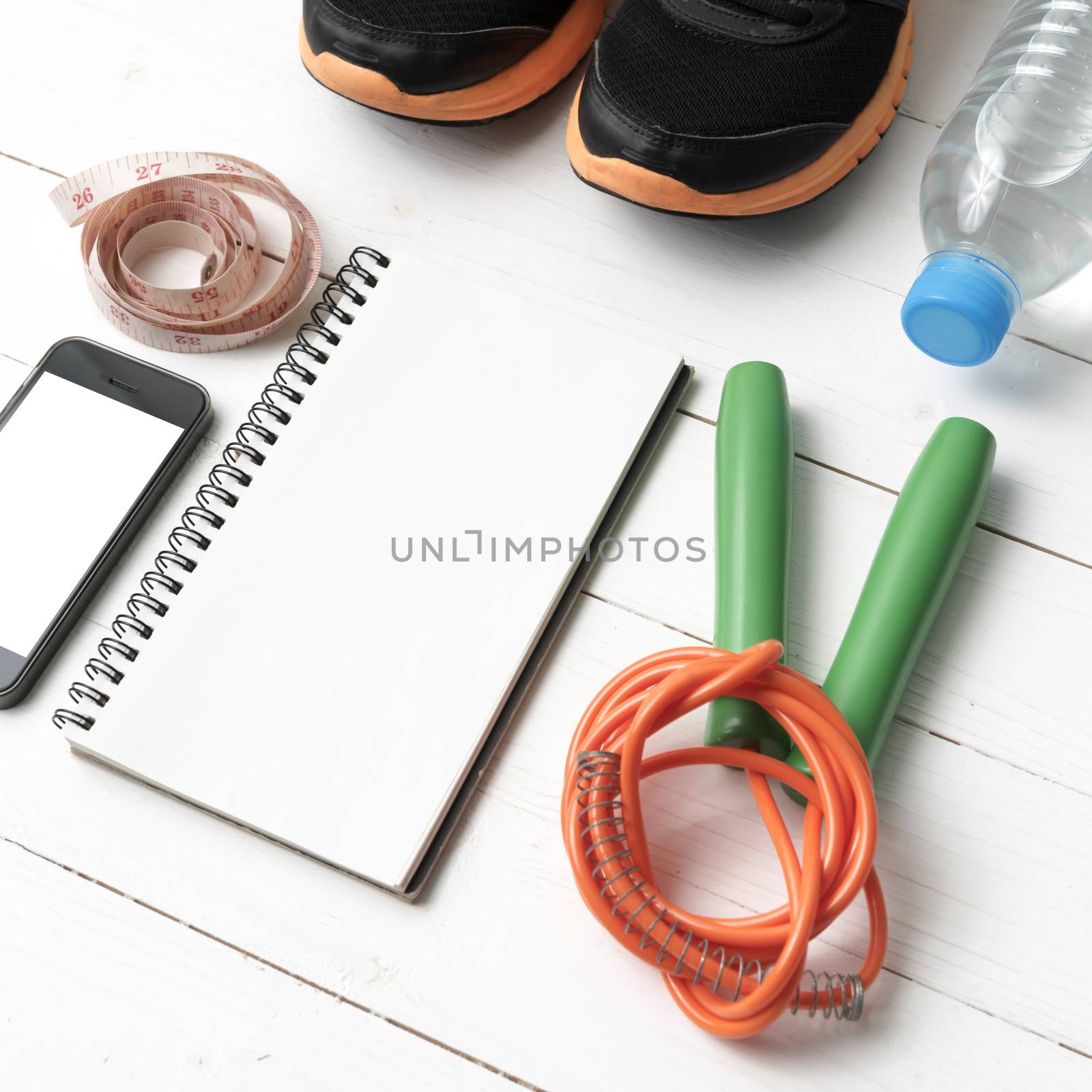 fitness equipment : running shoes,jumping rope,drinking water,notebook,measuring tape and phone on white wood table