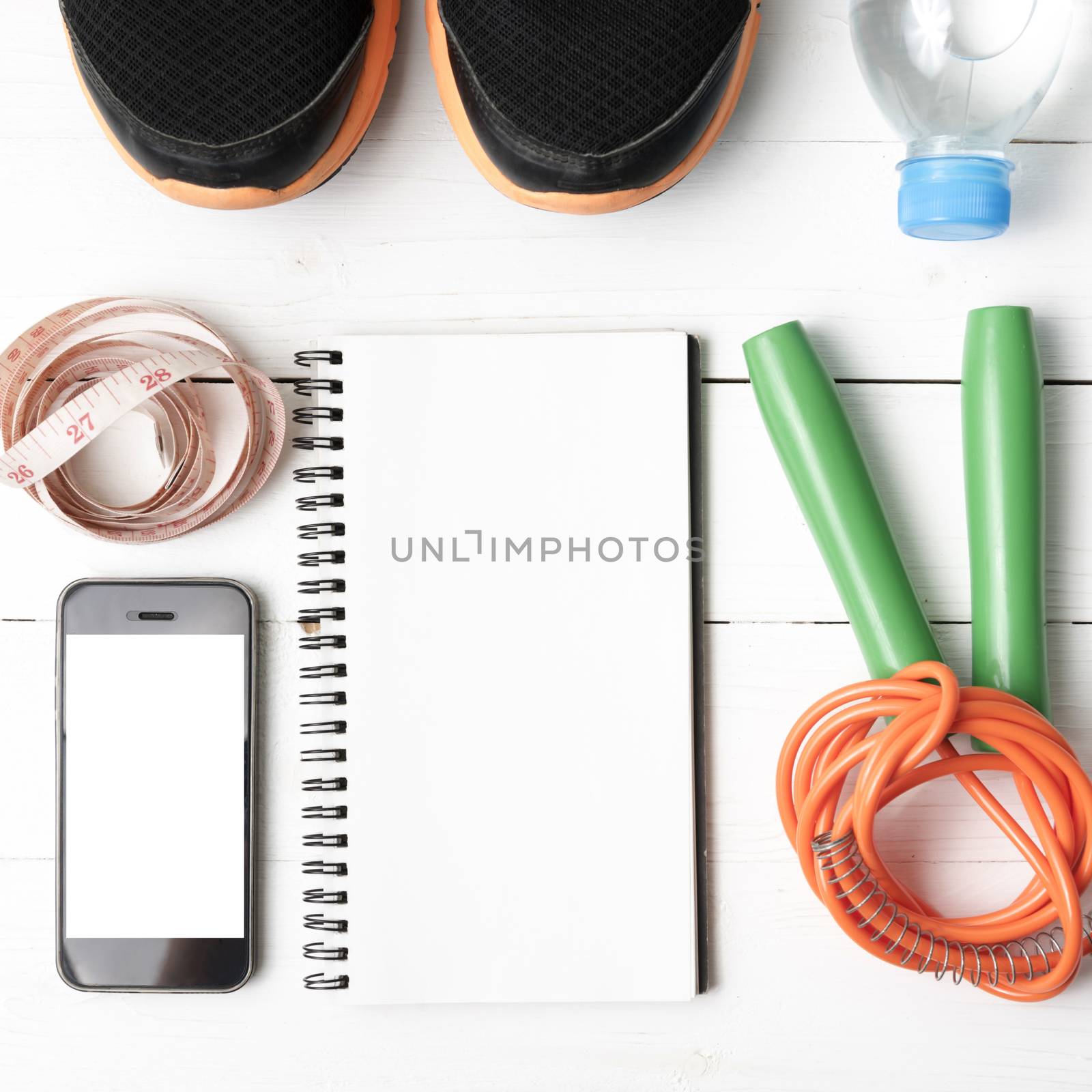 fitness equipment : running shoes,jumping rope,drinking water,notebook,measuring tape and phone on white wood table