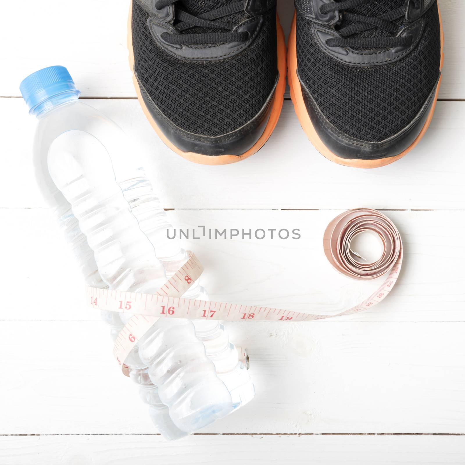 fitness equipment : running shoes,drinking water and measuring tape on white wood table