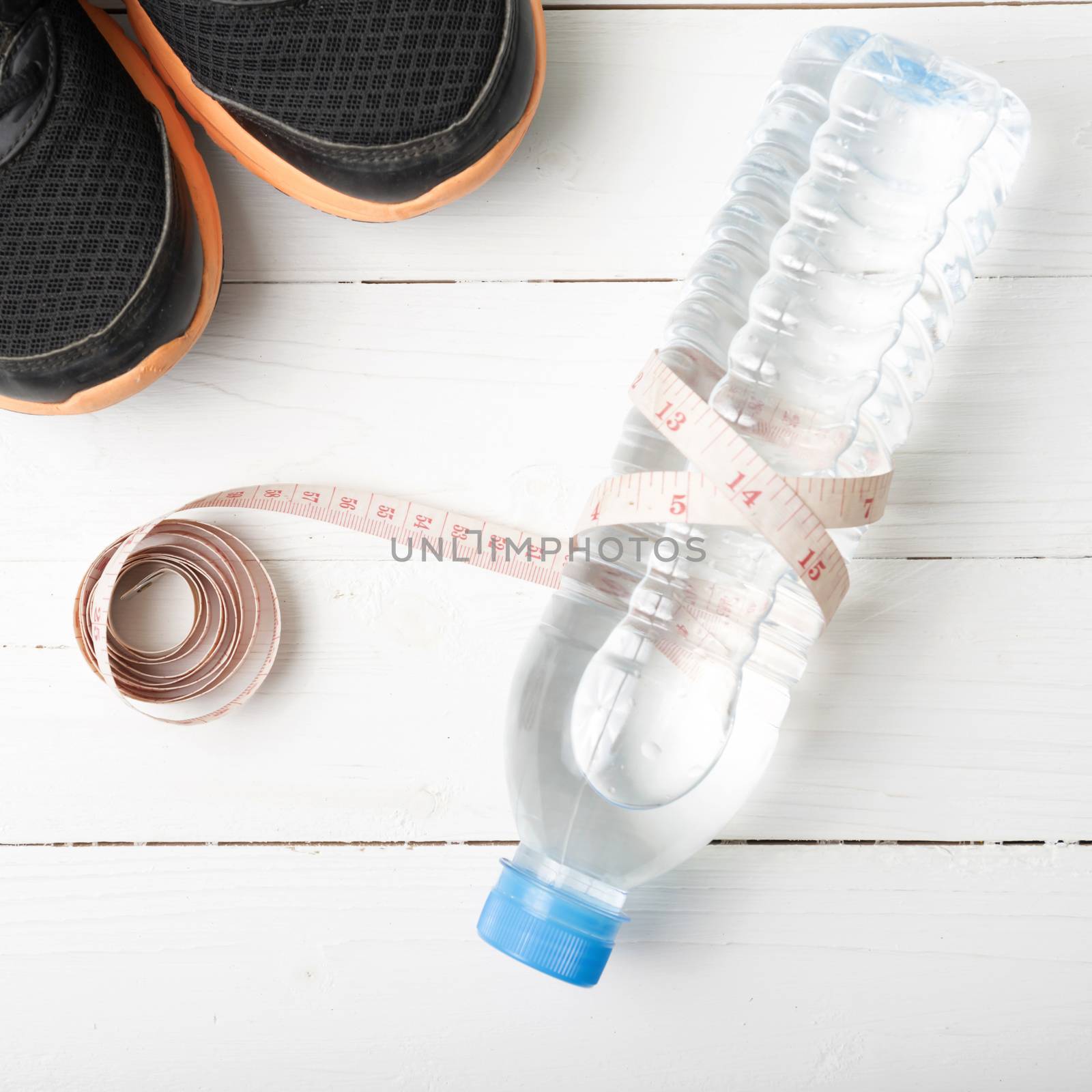 fitness equipment : running shoes,drinking water and measuring tape on white wood table