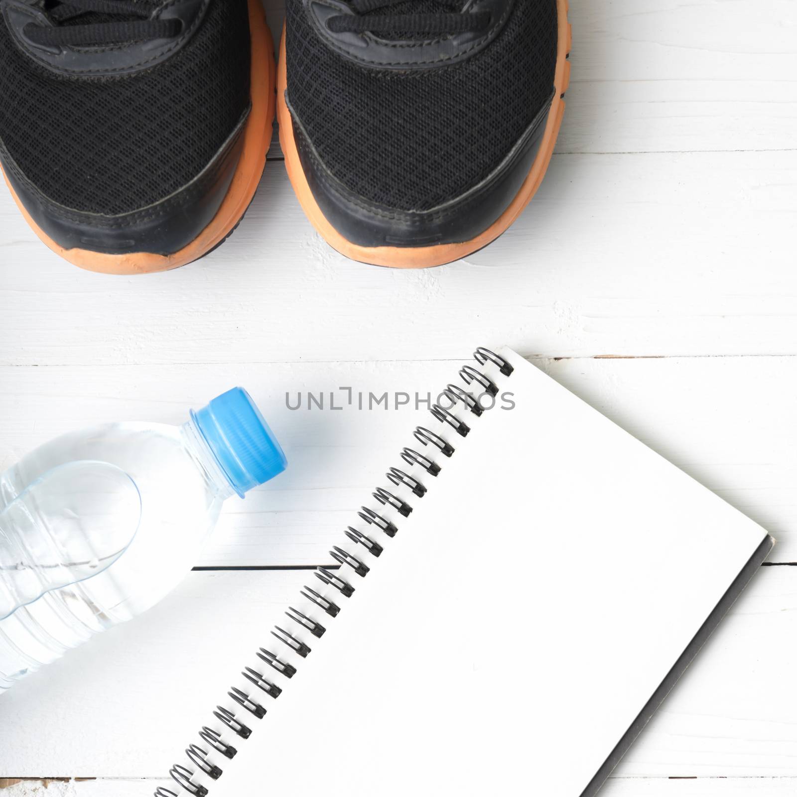 fitness equipment : running shoes,drinking water and notebook on white wood table