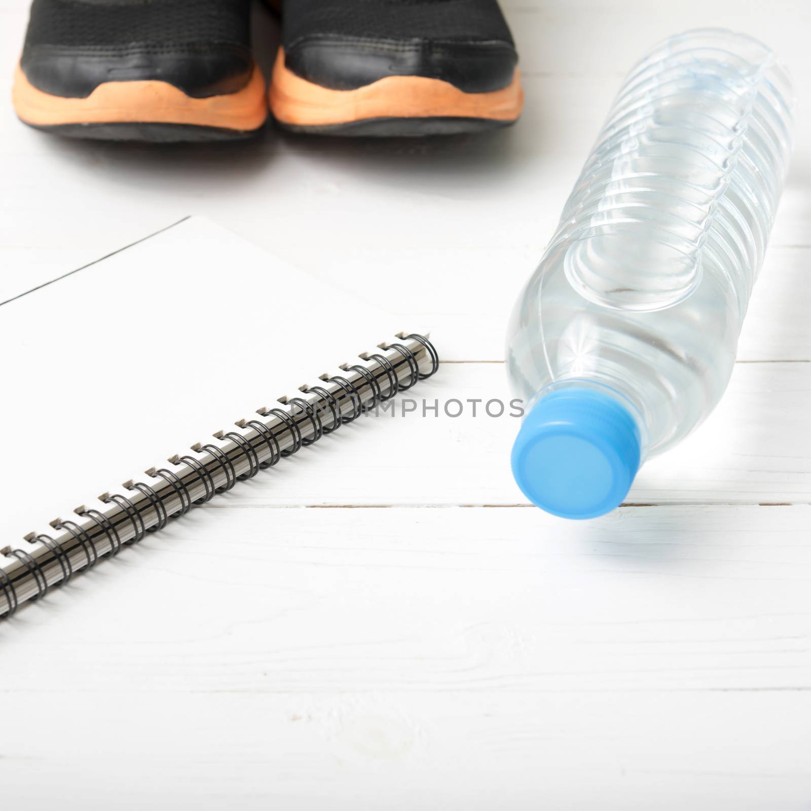 fitness equipment : running shoes,drinking water and notebook on white wood table