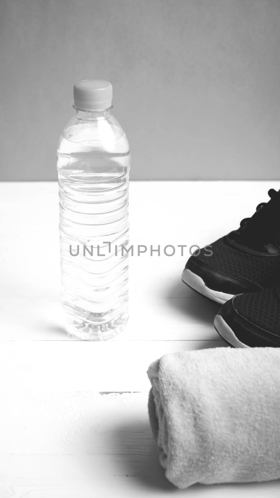 fitness equipment: towel,drinking water and running shoes on white wood table black and white color style