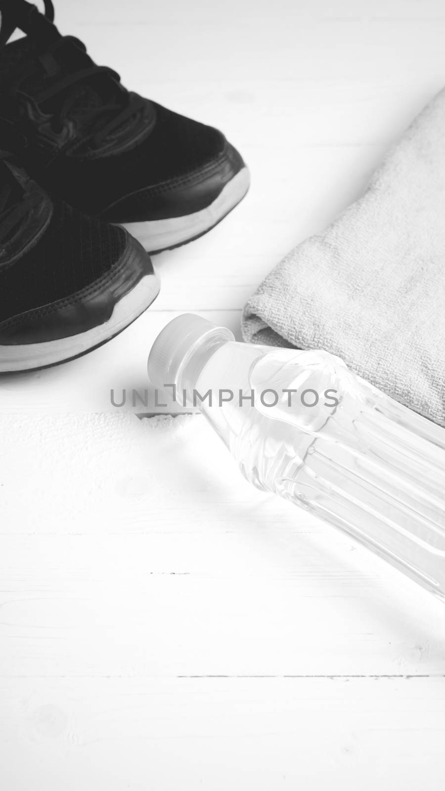 fitness equipment: towel,drinking water and running shoes on white wood table black and white color style