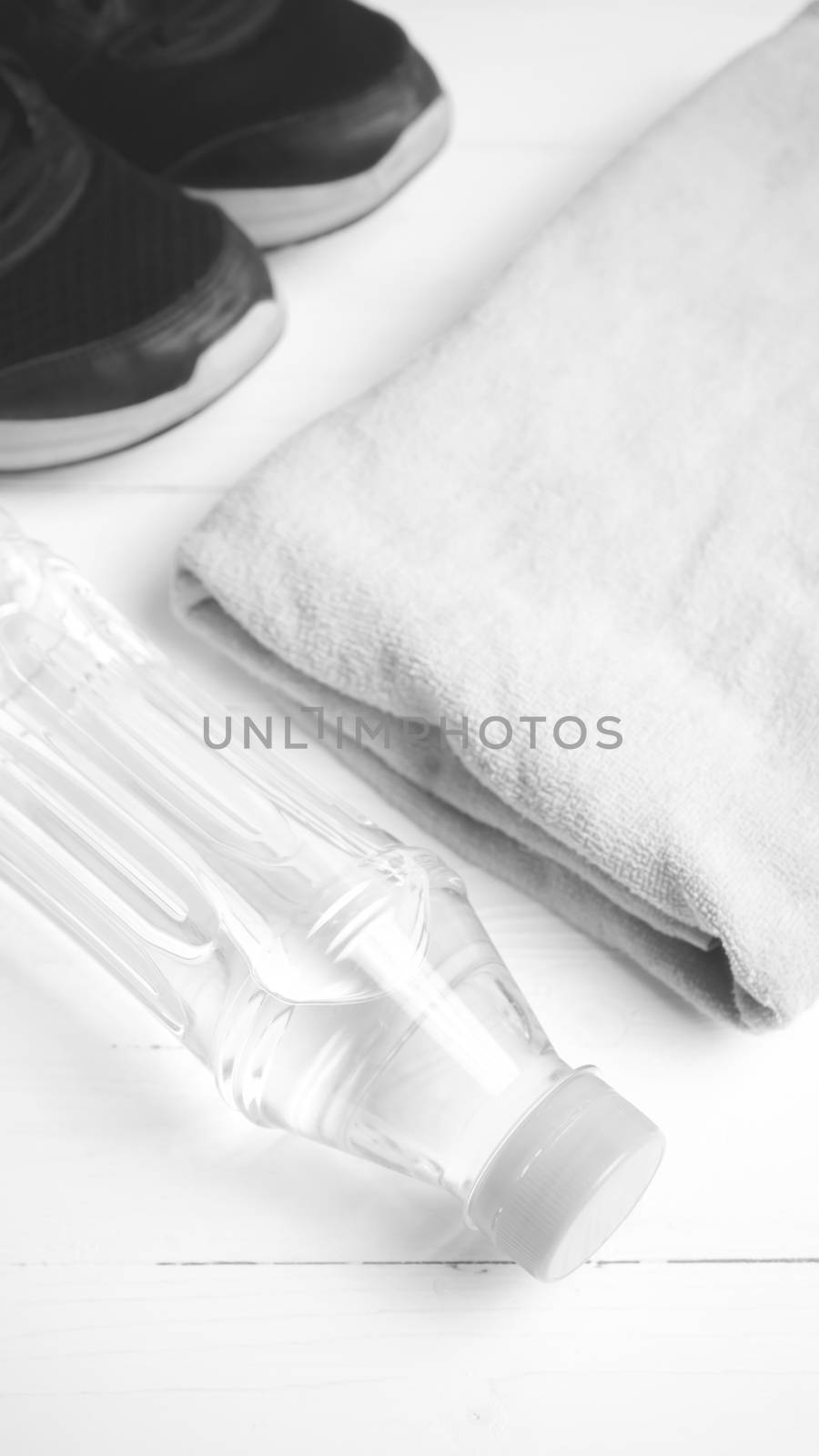 fitness equipment: towel,drinking water and running shoes on white wood table black and white color style