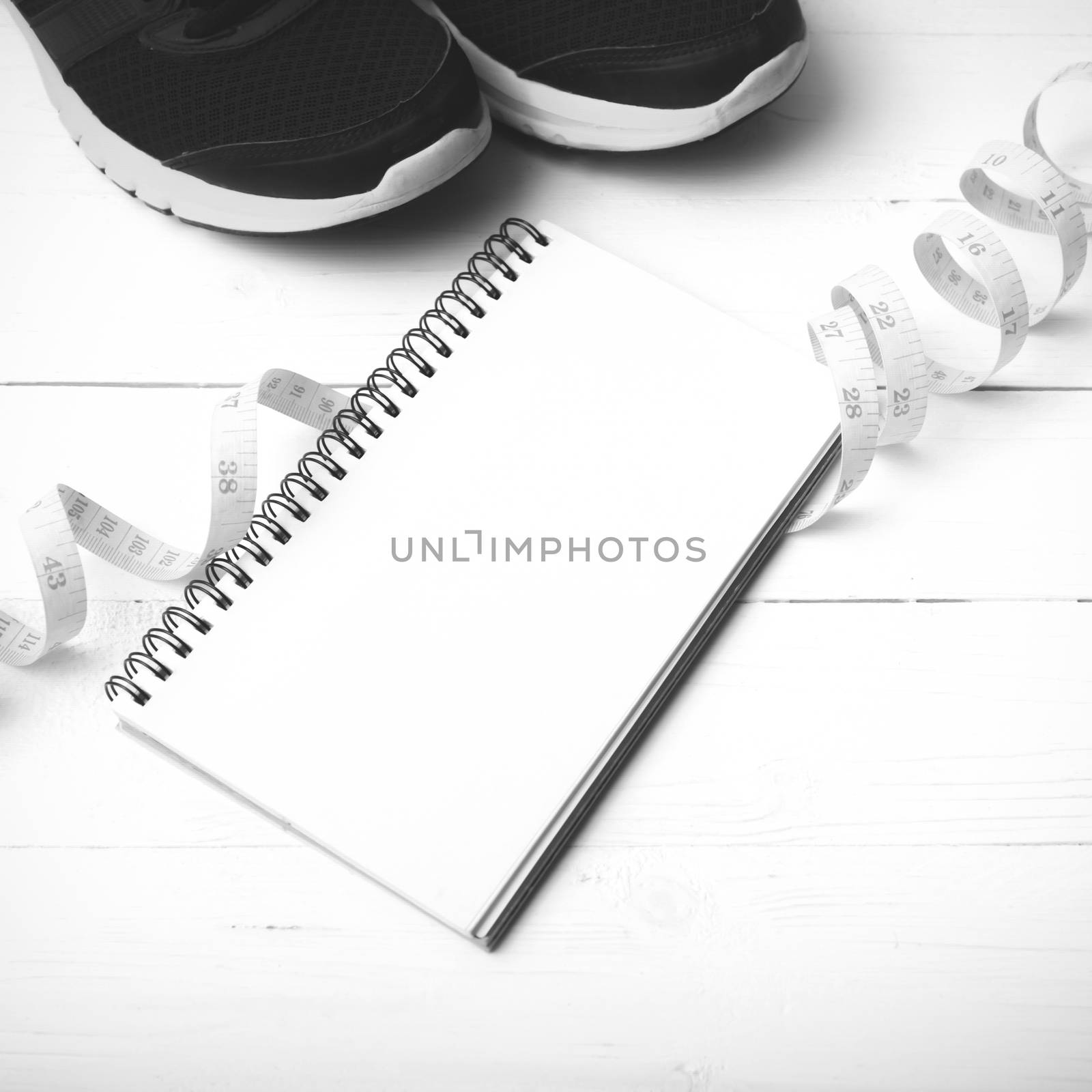 running shoes with notebook and measuring tape on white wood table black and white tone color style