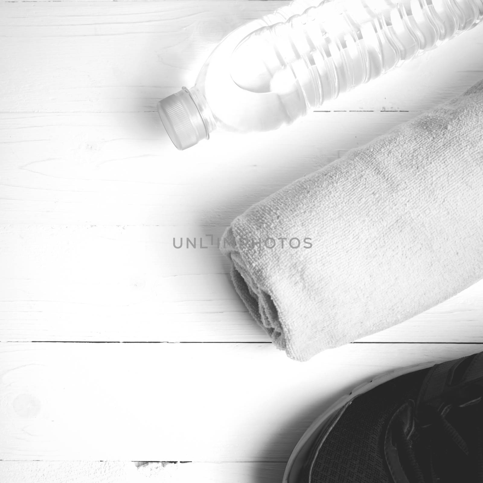 fitness equipment: towel,drinking water and running shoes on white wood table black and white color style