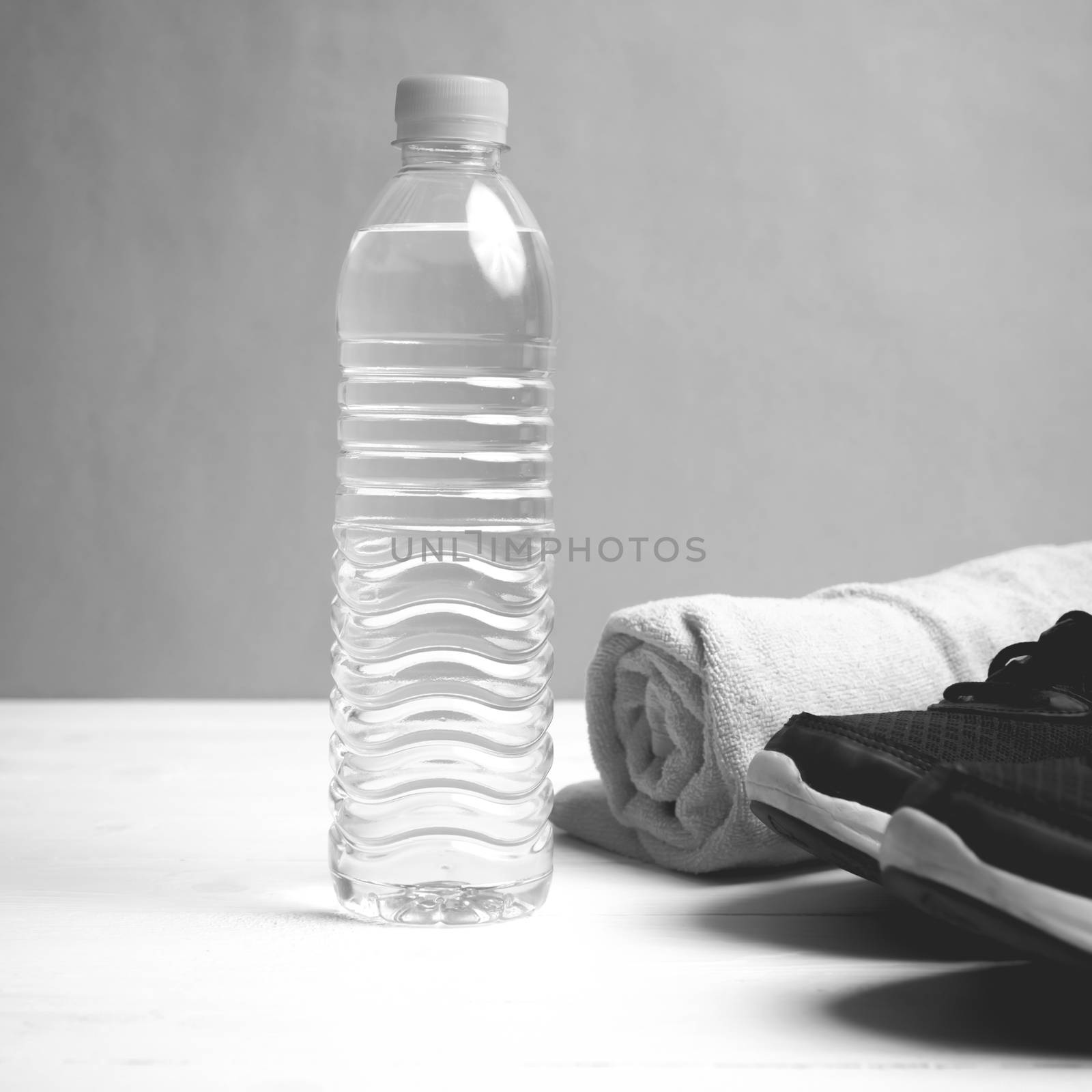 fitness equipment: towel,drinking water and running shoes on white wood table black and white color style