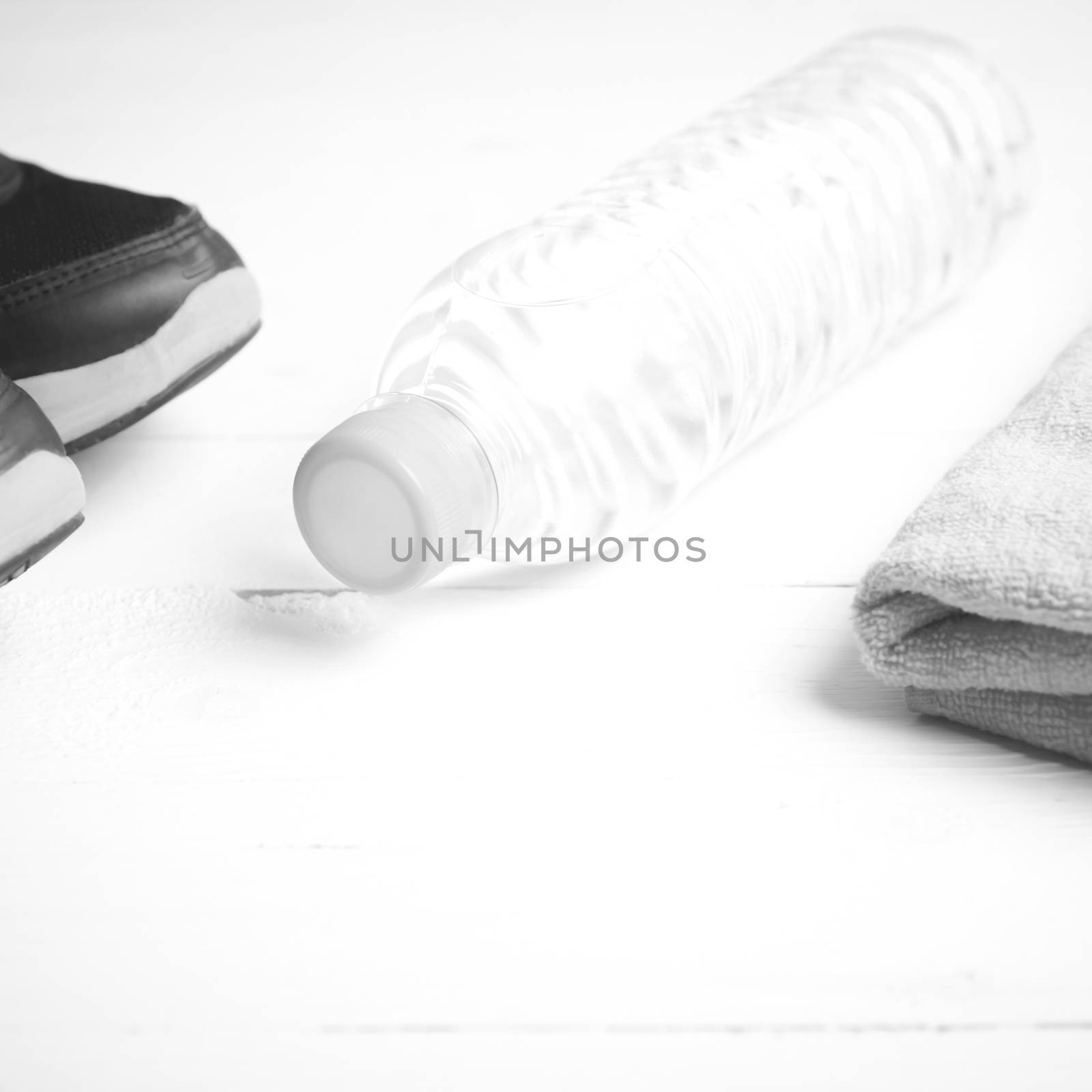 fitness equipment: towel,drinking water and running shoes on white wood table black and white color style