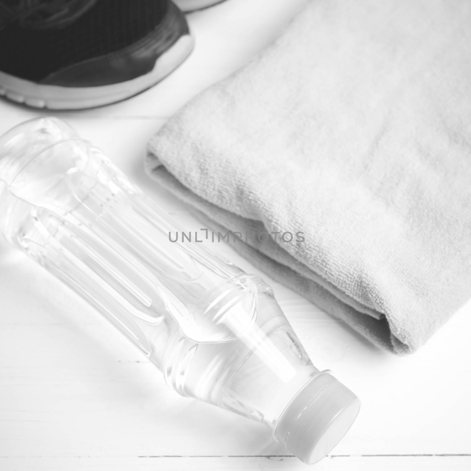 fitness equipment: towel,drinking water and running shoes on white wood table black and white color style