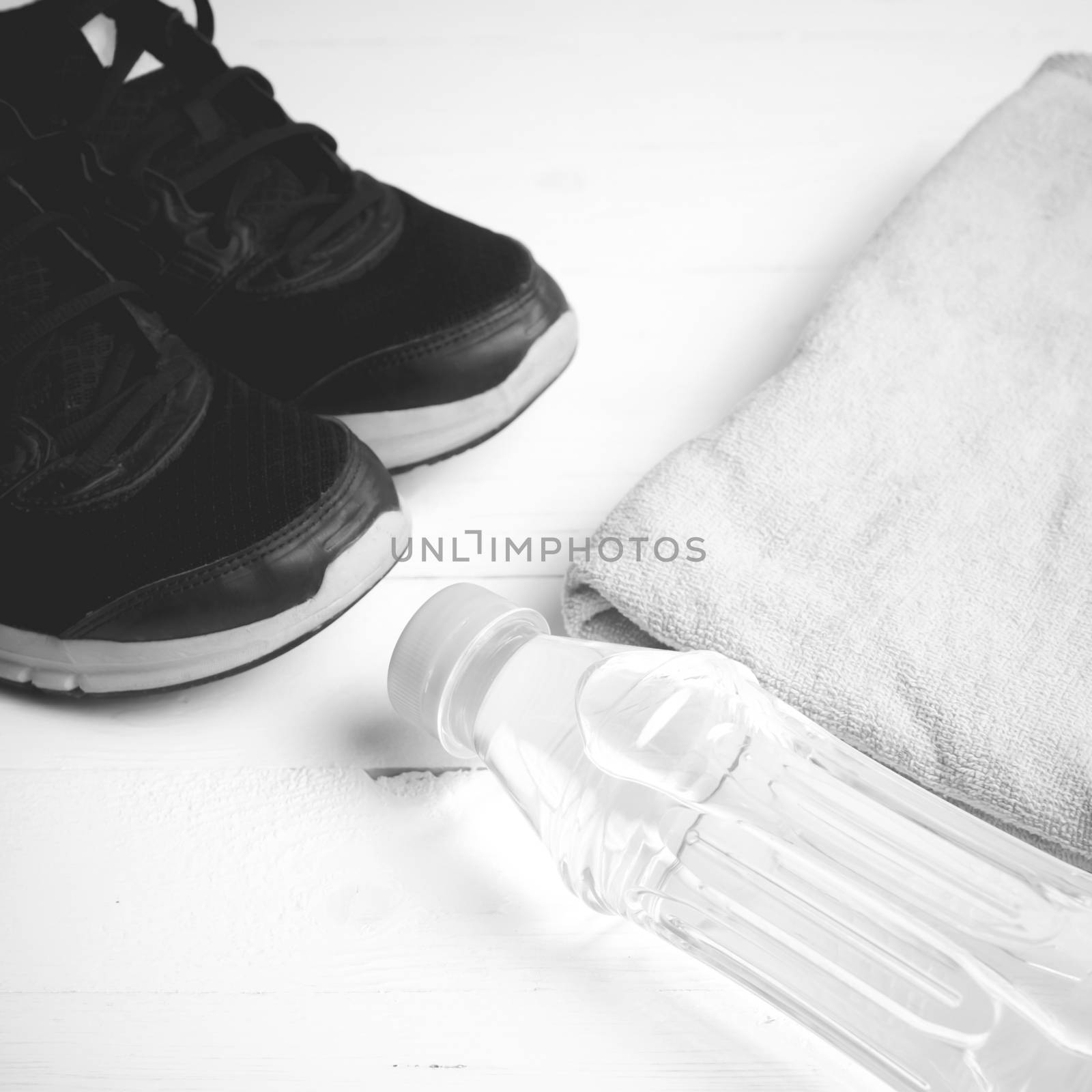 fitness equipment: towel,drinking water and running shoes on white wood table black and white color style