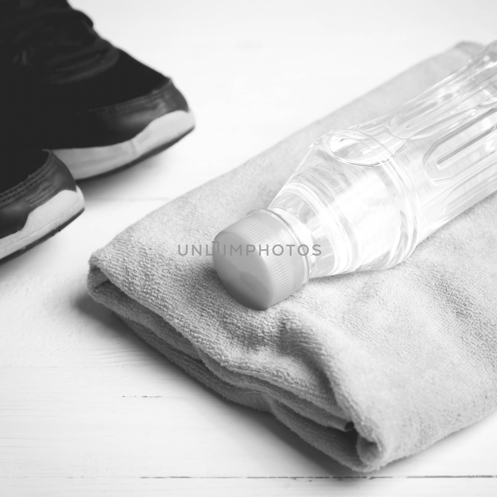 fitness equipment: towel,drinking water and running shoes on white wood table black and white color style