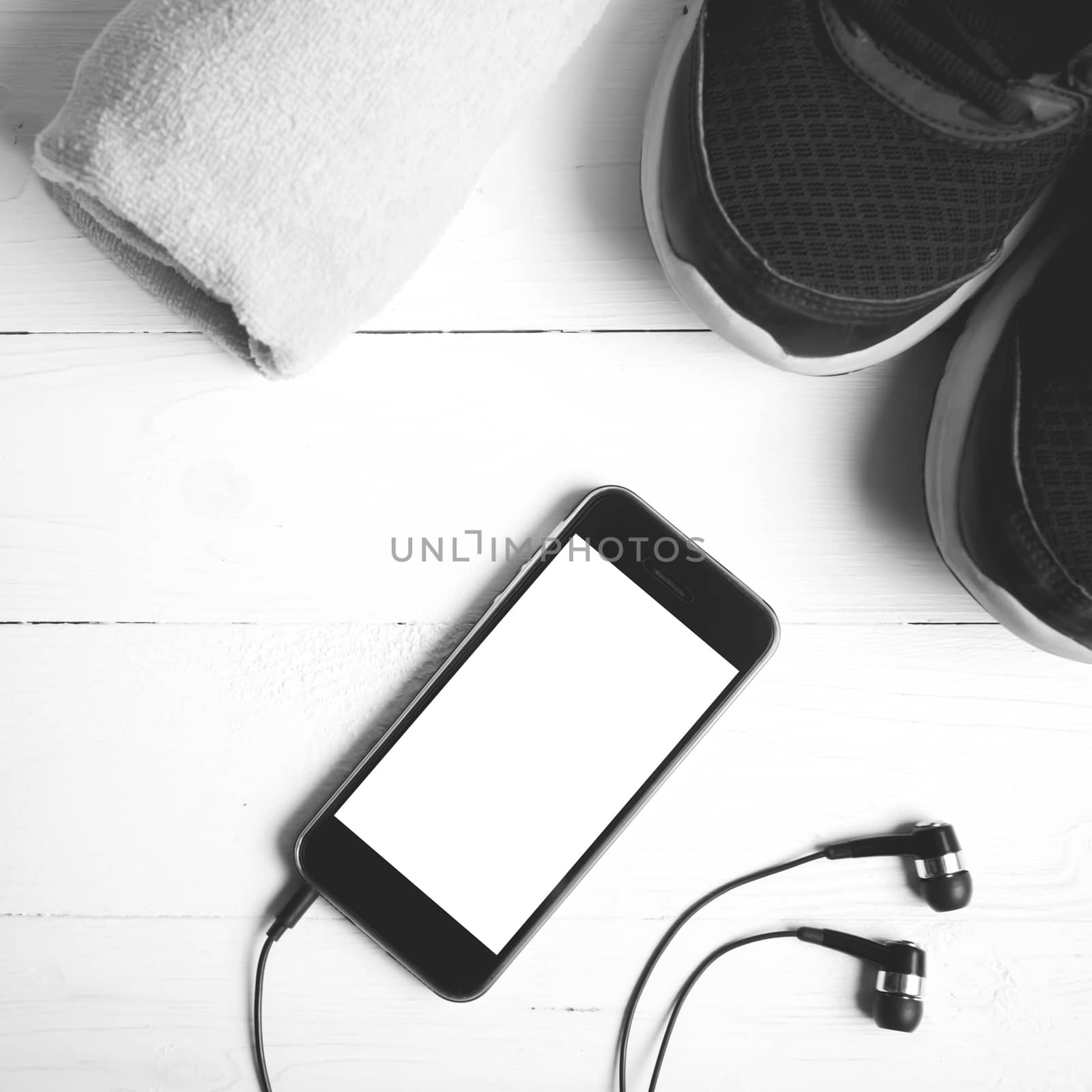 fitness equipment:running shoes,towel and smart phone on white wood table black and white color style