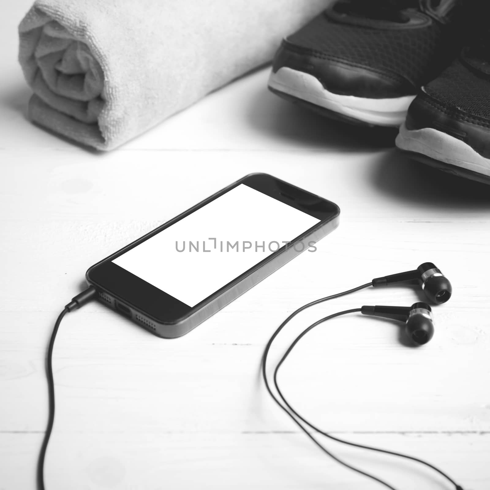 fitness equipment:running shoes,towel and smart phone on white wood table black and white color style